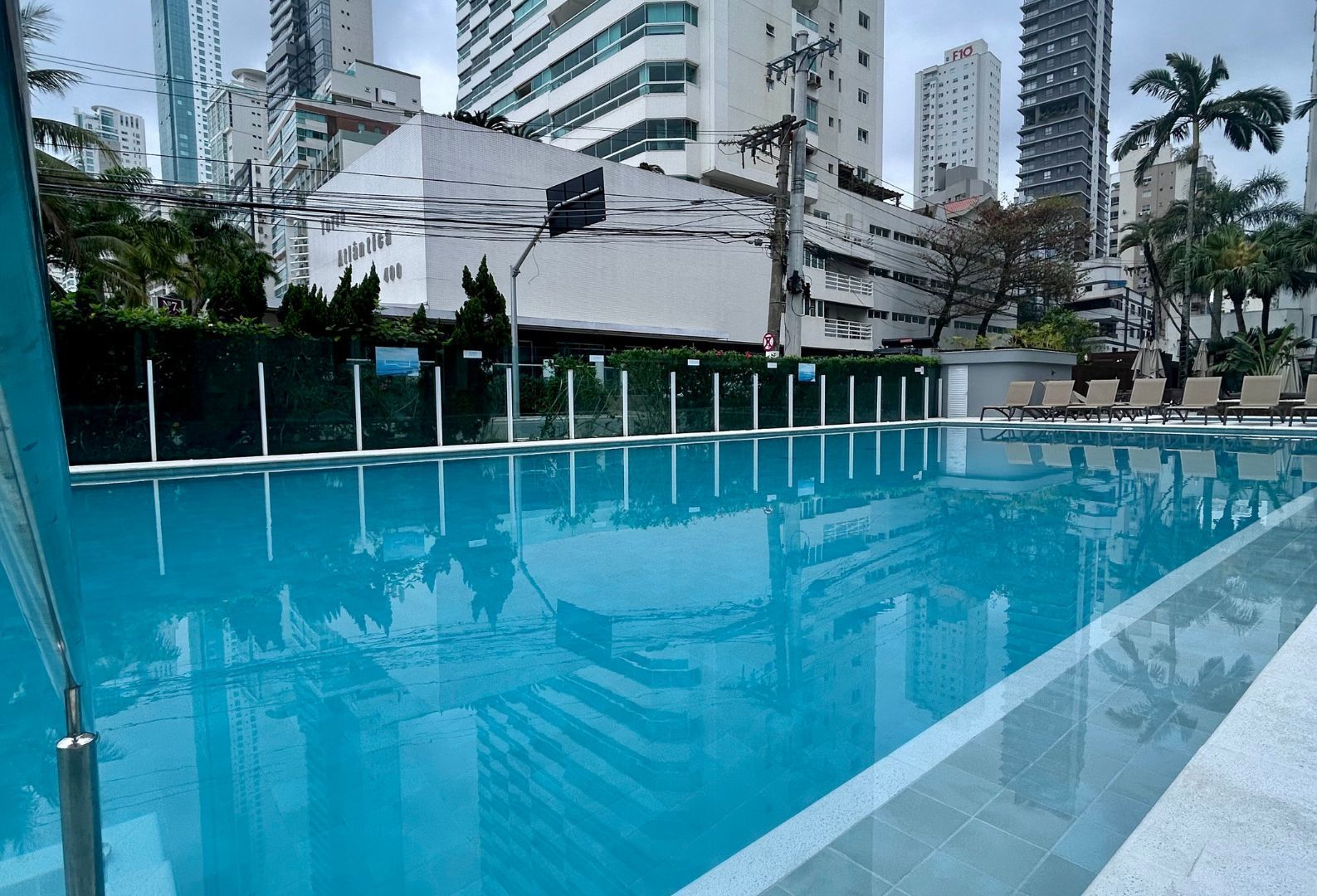Piscina ao ar livre com água azul cristalina ao lado de prédios altos e palmeiras.