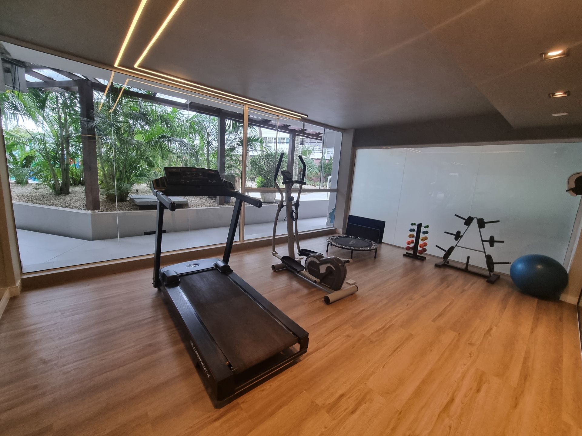 Academia moderna com esteiras, pesos e bola de exercícios em uma sala iluminada com janelas amplas.