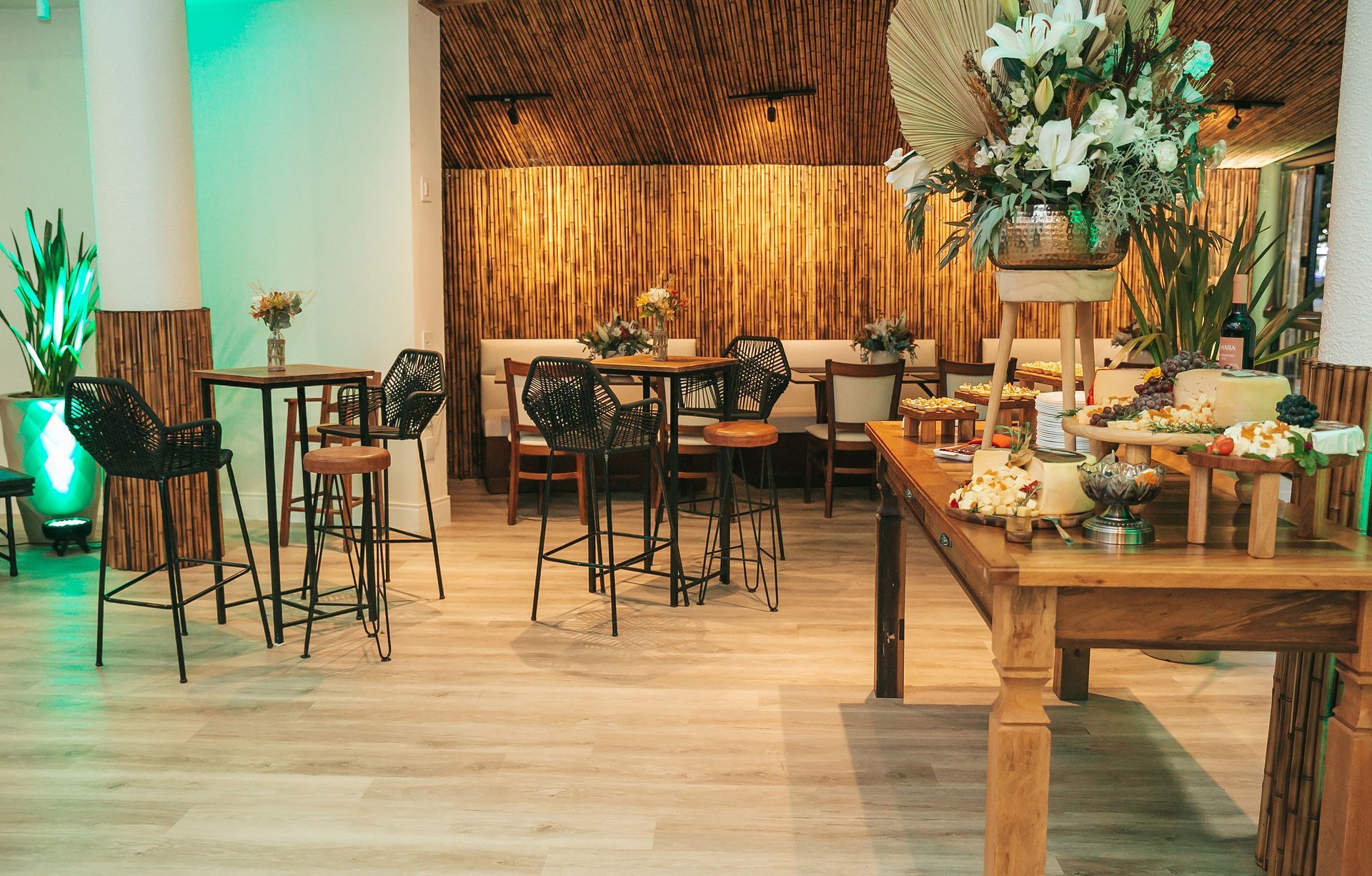Elegante salão de banquetes com mesas redondas, piso de madeira e arranjos florais, iluminado por uma luz verde aconchegante.