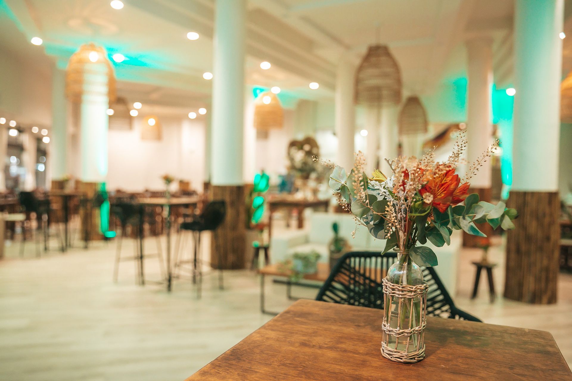 Elegante salão de banquetes com colunas brancas, iluminação aconchegante e um arranjo de flores sobre uma mesa de madeira.