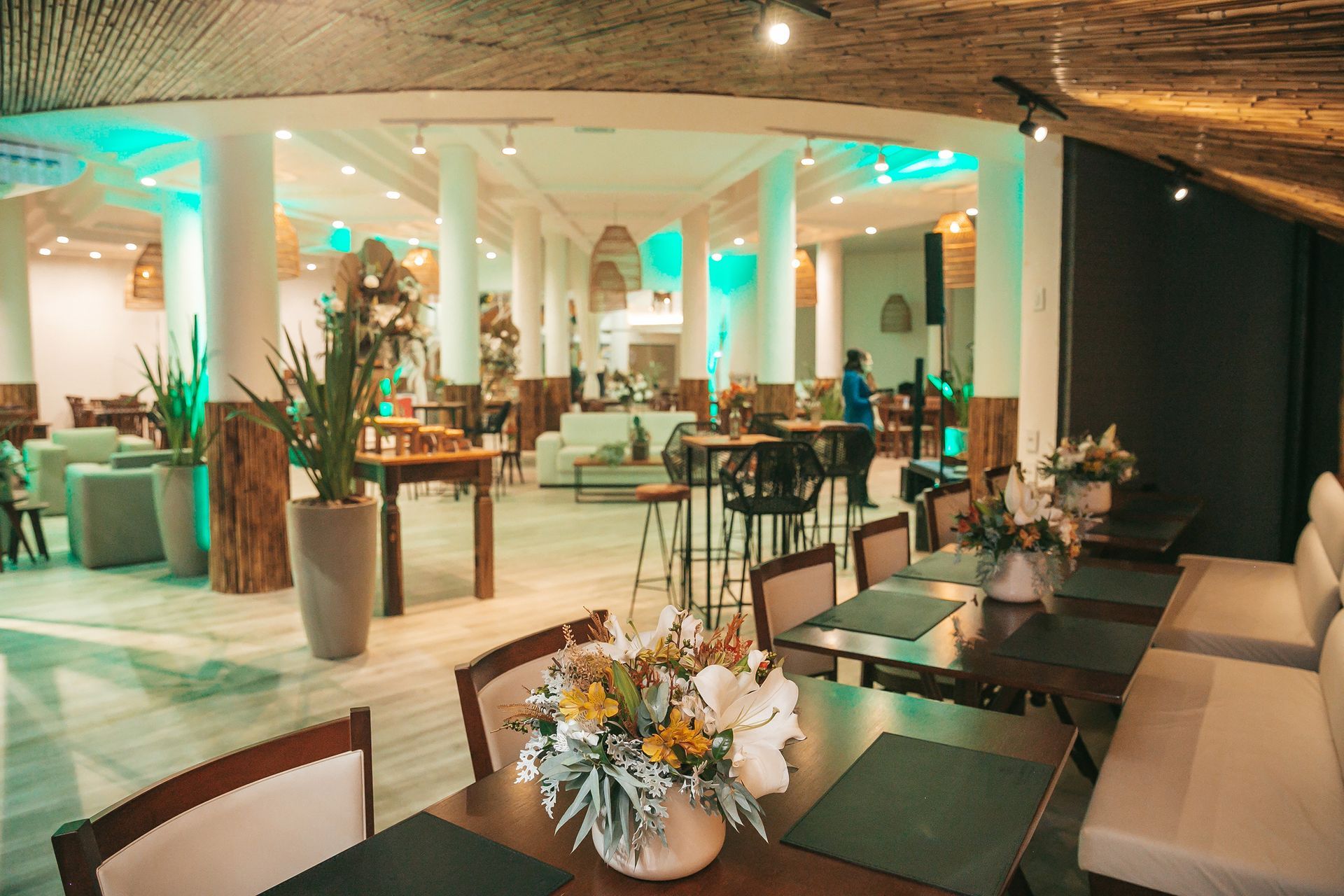 Elegante espaço para eventos internos com colunas brancas, iluminação verde e mesas e áreas de estar decoradas.