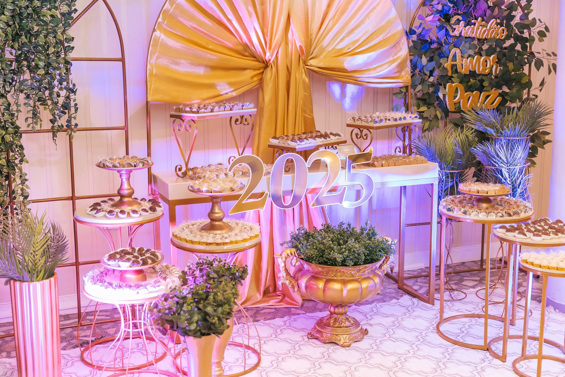 Decoração de aniversário em tons de rosa pastel e dourado com balões, bolos, suportes e arranjos florais.