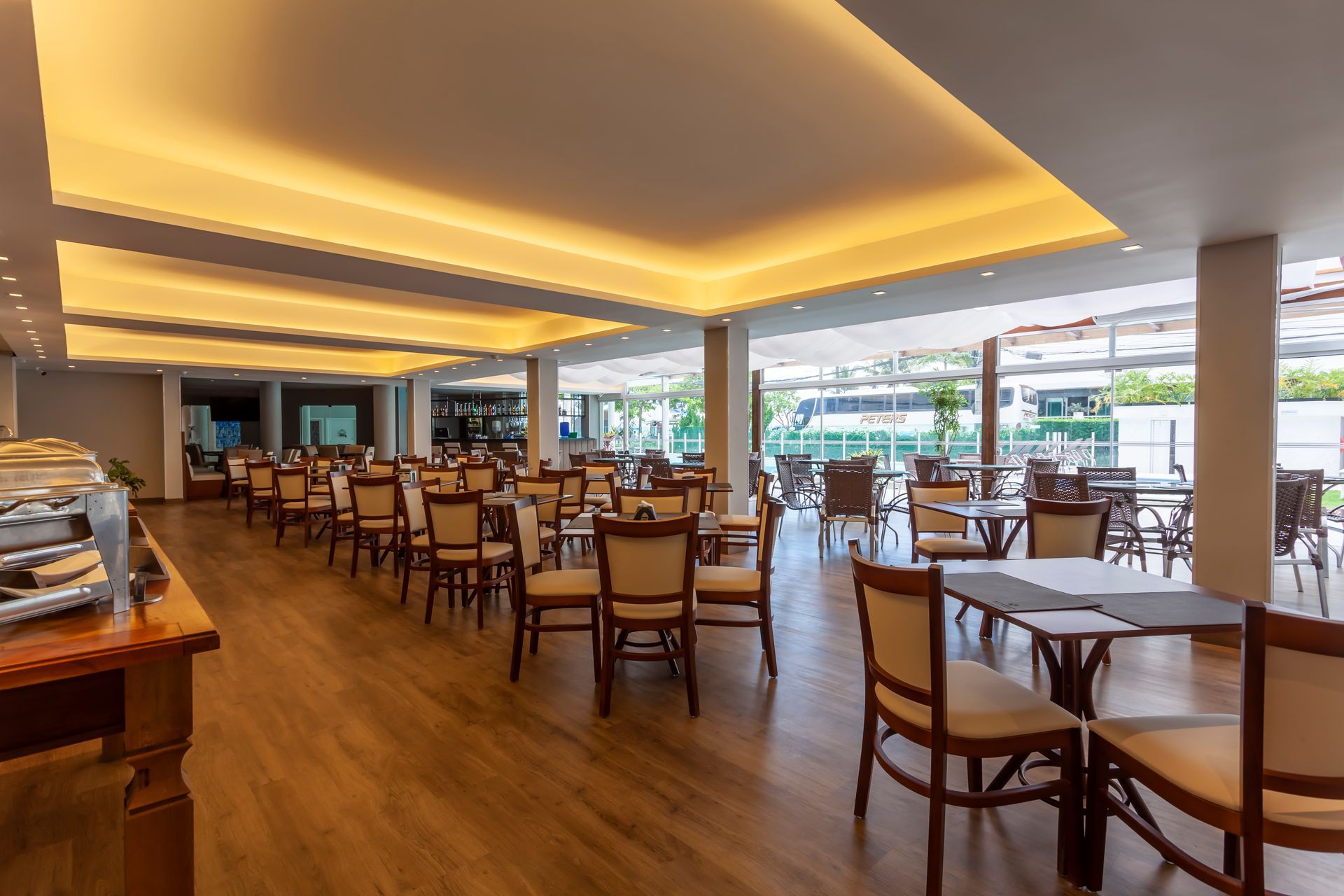 Sala de jantar espaçosa e moderna, com mesas e cadeiras de madeira e iluminação aconchegante no teto.