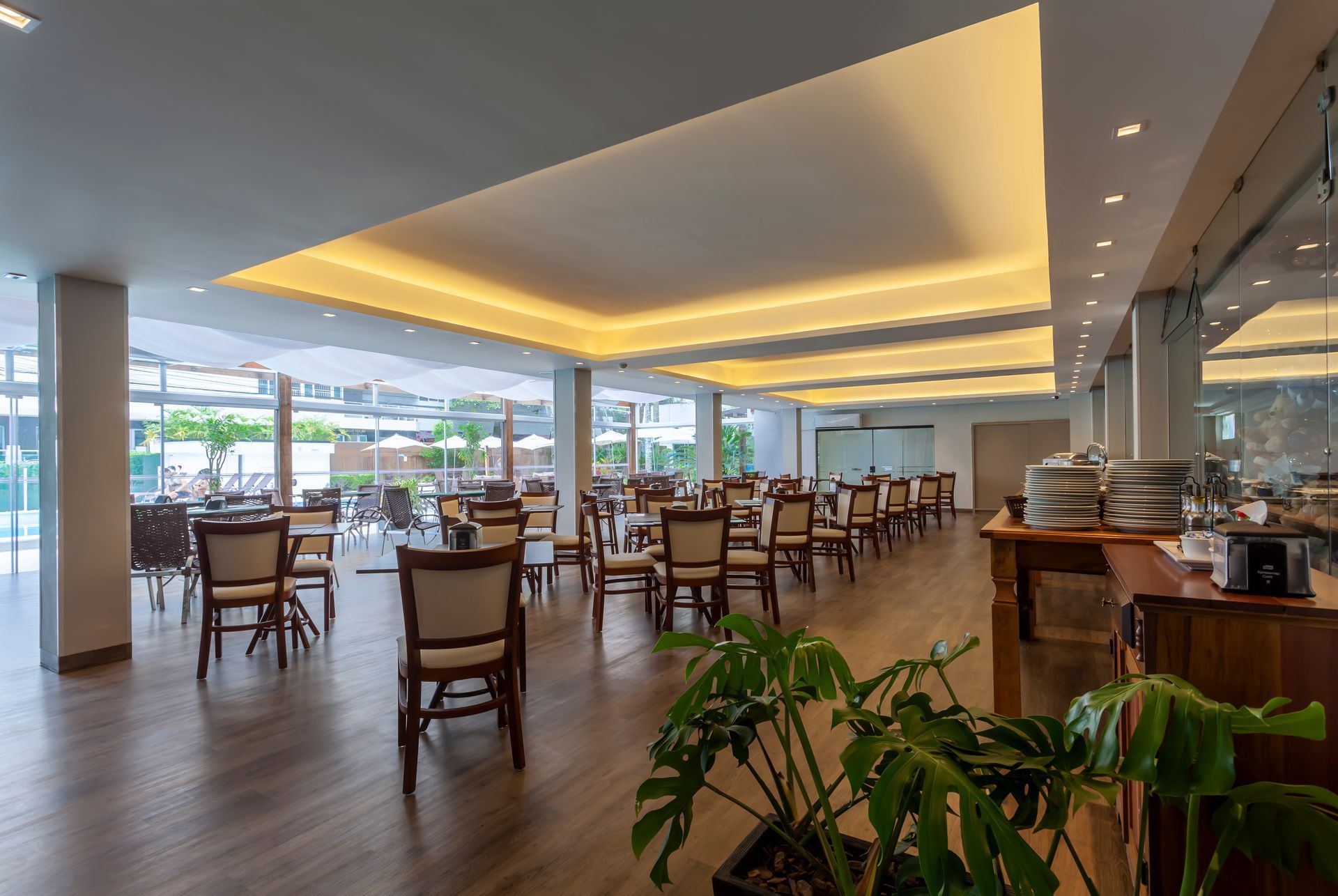 Restaurante moderno e luminoso com mesas e cadeiras de madeira vazias e uma ampla área de jantar com janelas.
