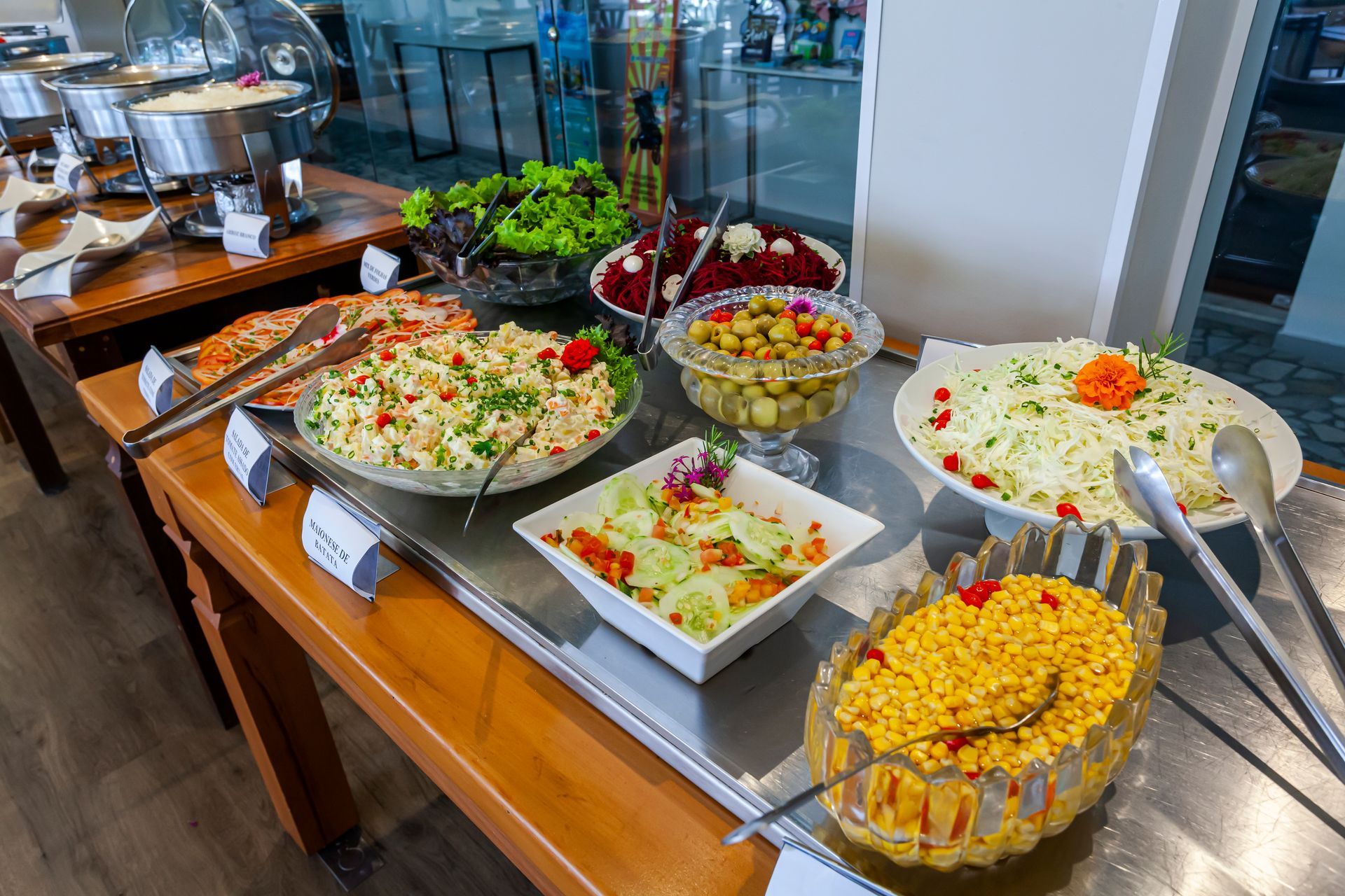 Mesa de bufê com saladas variadas e acompanhamentos em tigelas e bandejas, incluindo arroz, verduras e legumes mistos.