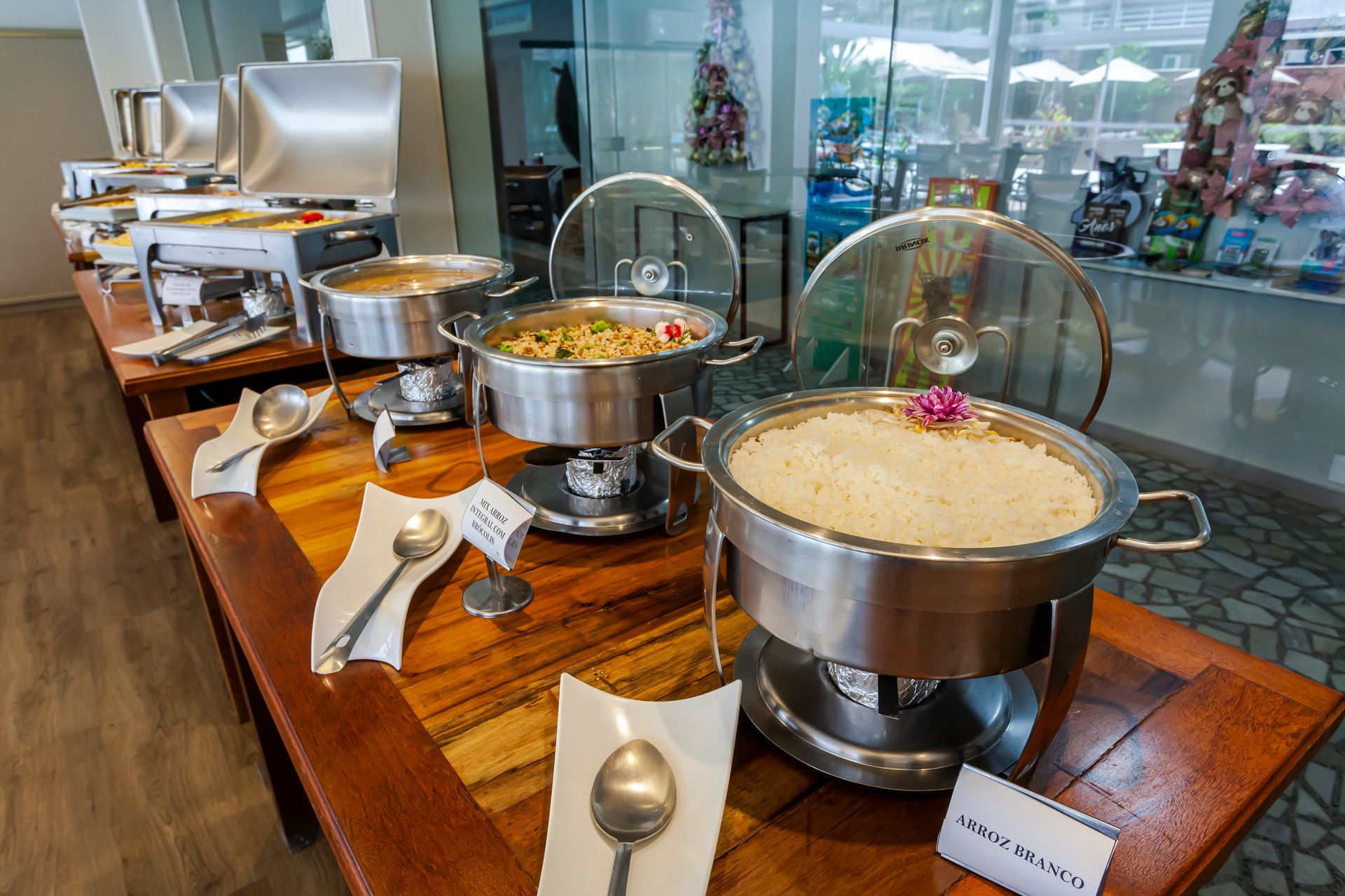 Mesa de buffet com rechauds de prata e tigelas de comida no saguão de um restaurante.