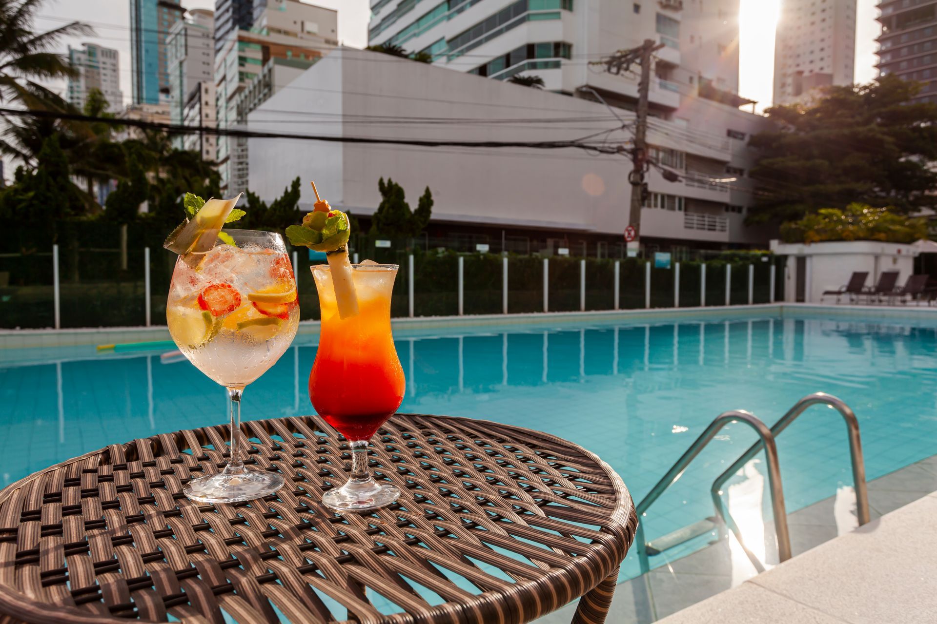 Duas bebidas coloridas sobre uma mesa de vime junto à piscina no terraço ao pôr do sol.