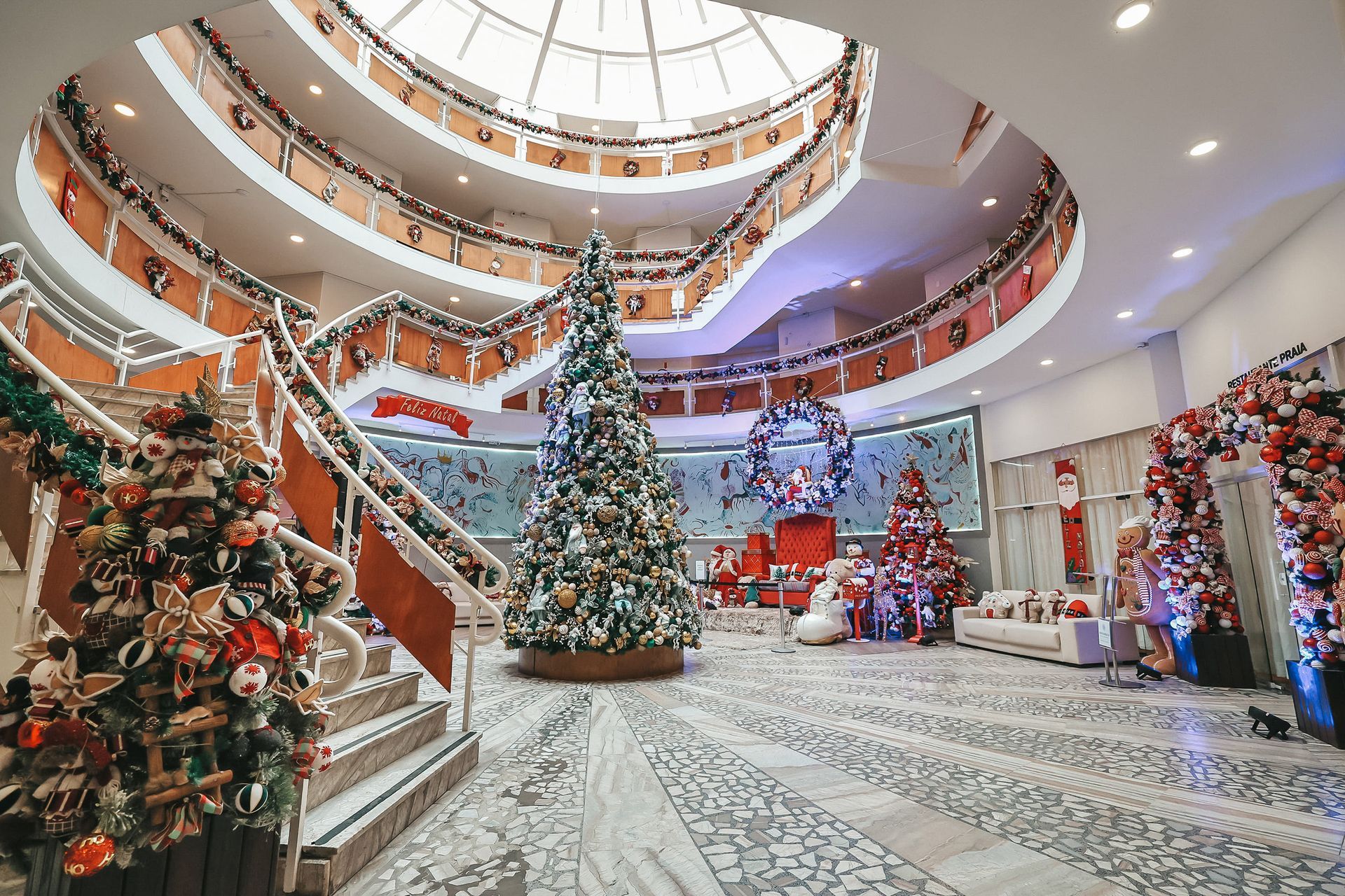 Átrio do shopping decorado festivamente com uma grande árvore de Natal e enfeites natalinos.