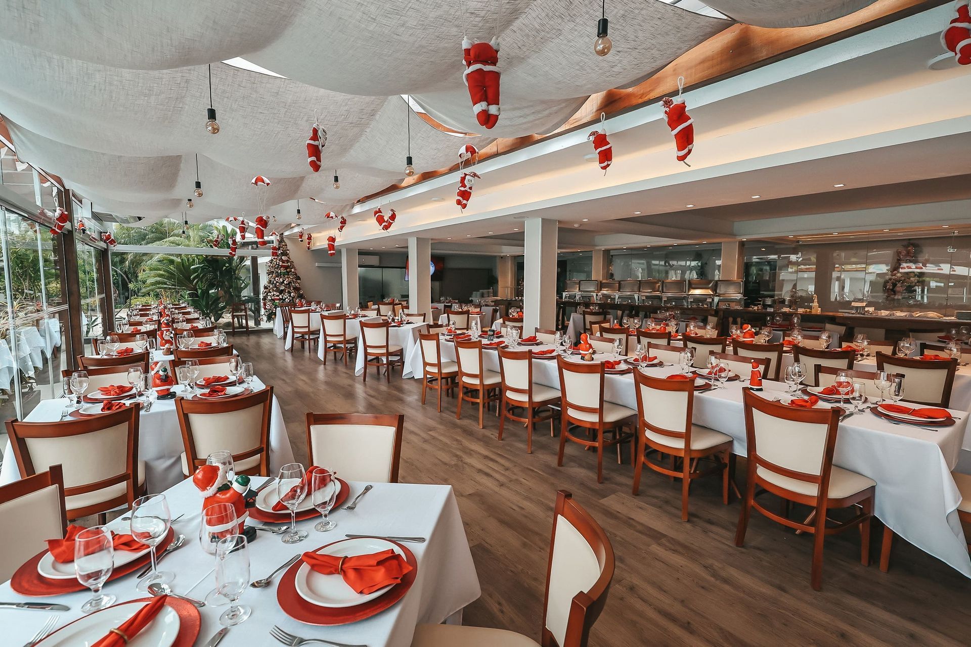 Sala de jantar elegante de restaurante com toalhas de mesa brancas, guardanapos vermelhos e cadeiras de madeira sob decoração vermelha suspensa.