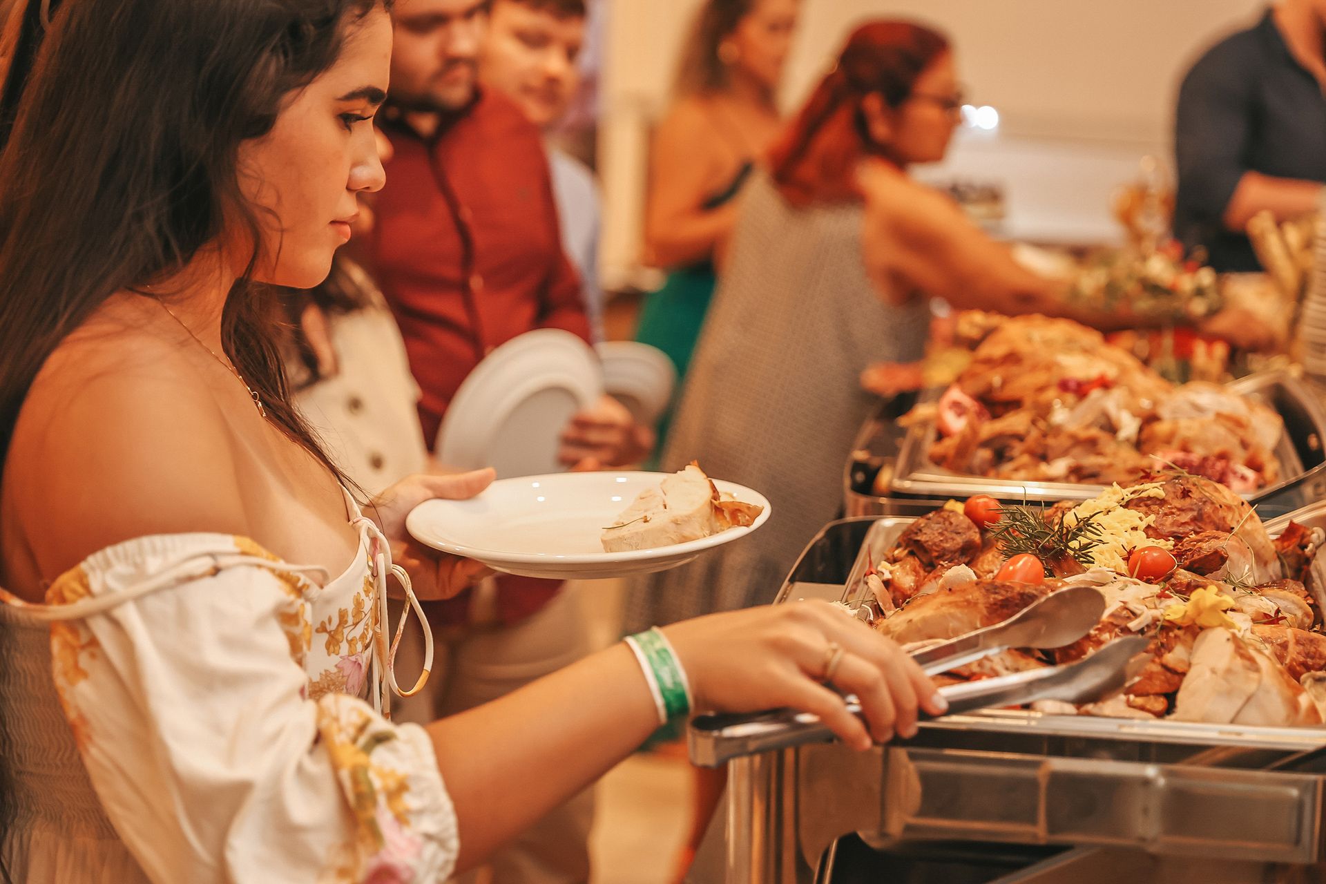 Mulher servindo comida de um bufê em um evento lotado em local fechado.