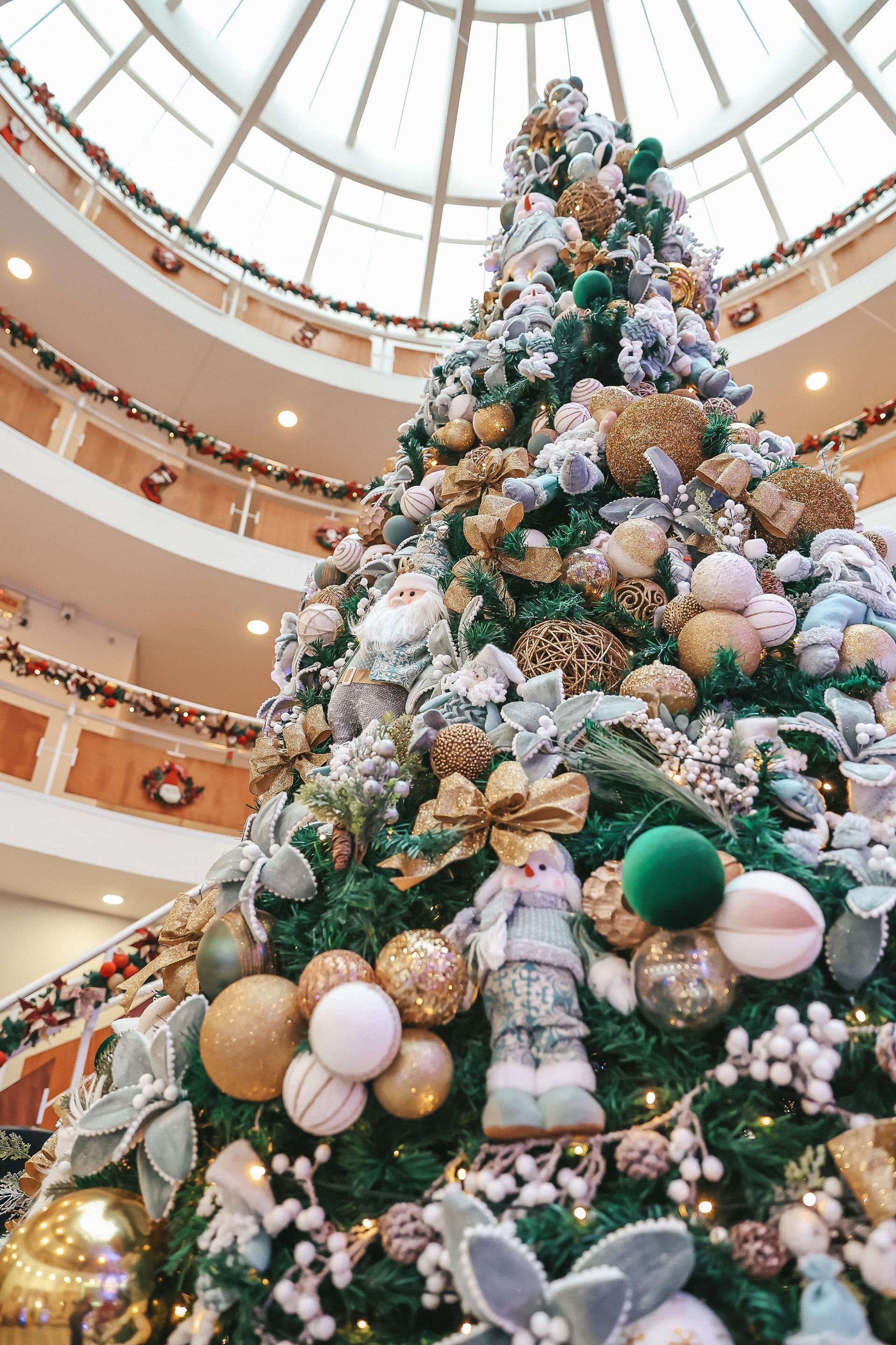 Árvore de Natal alta e decorada com enfeites brancos e dourados no átrio de um shopping center.