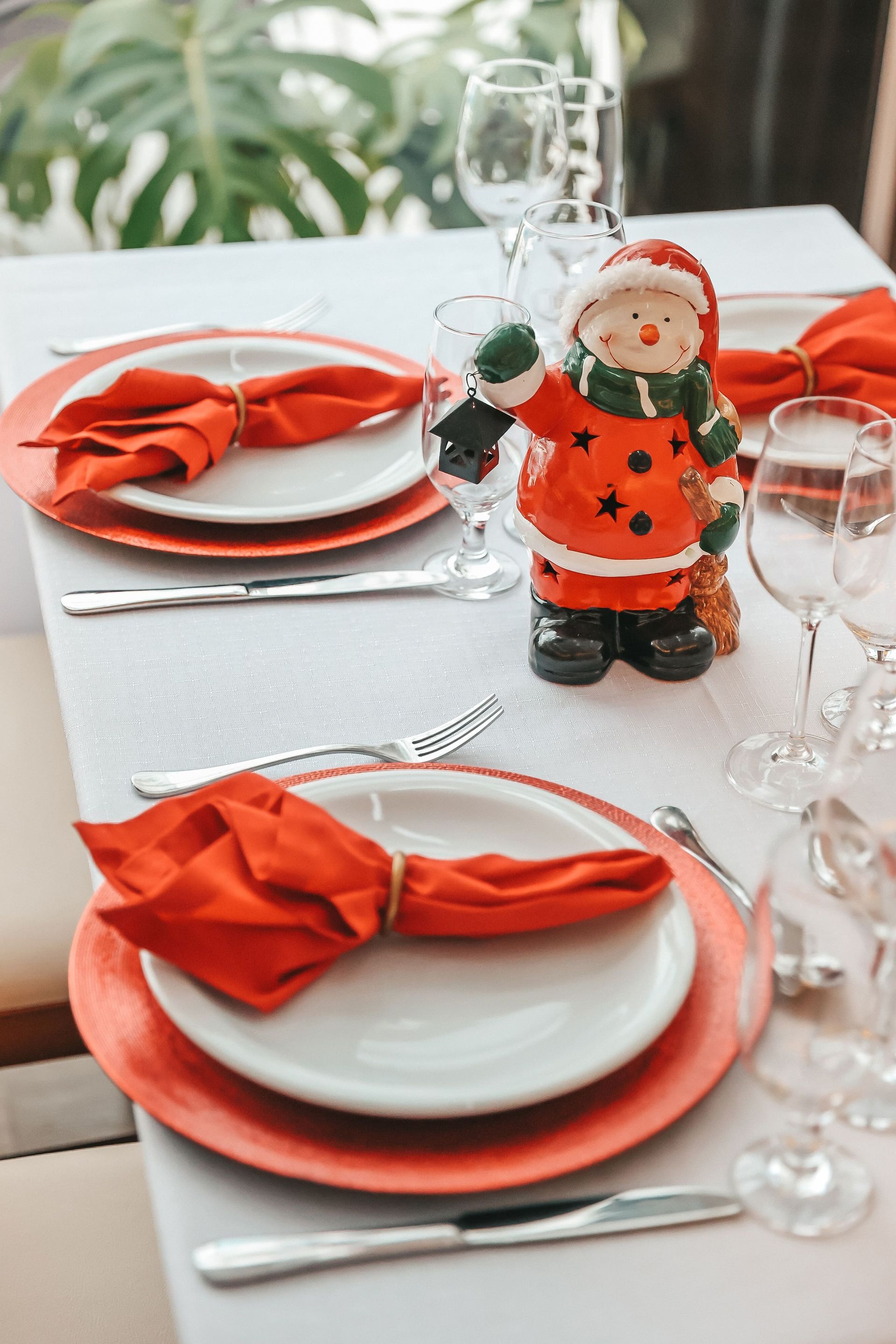 Decoração de mesa natalina com guardanapos vermelhos, pratos e uma pequena estatueta de Papai Noel como centro de mesa.