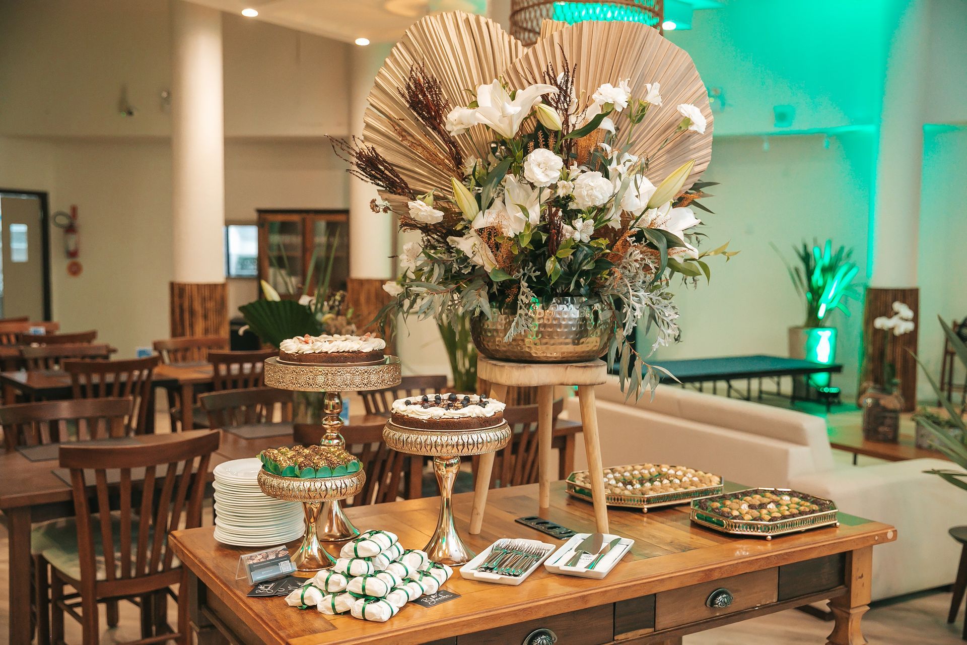 Mesa de sobremesas decorada com arranjo floral e doces variados em um salão de banquetes com iluminação aconchegante.