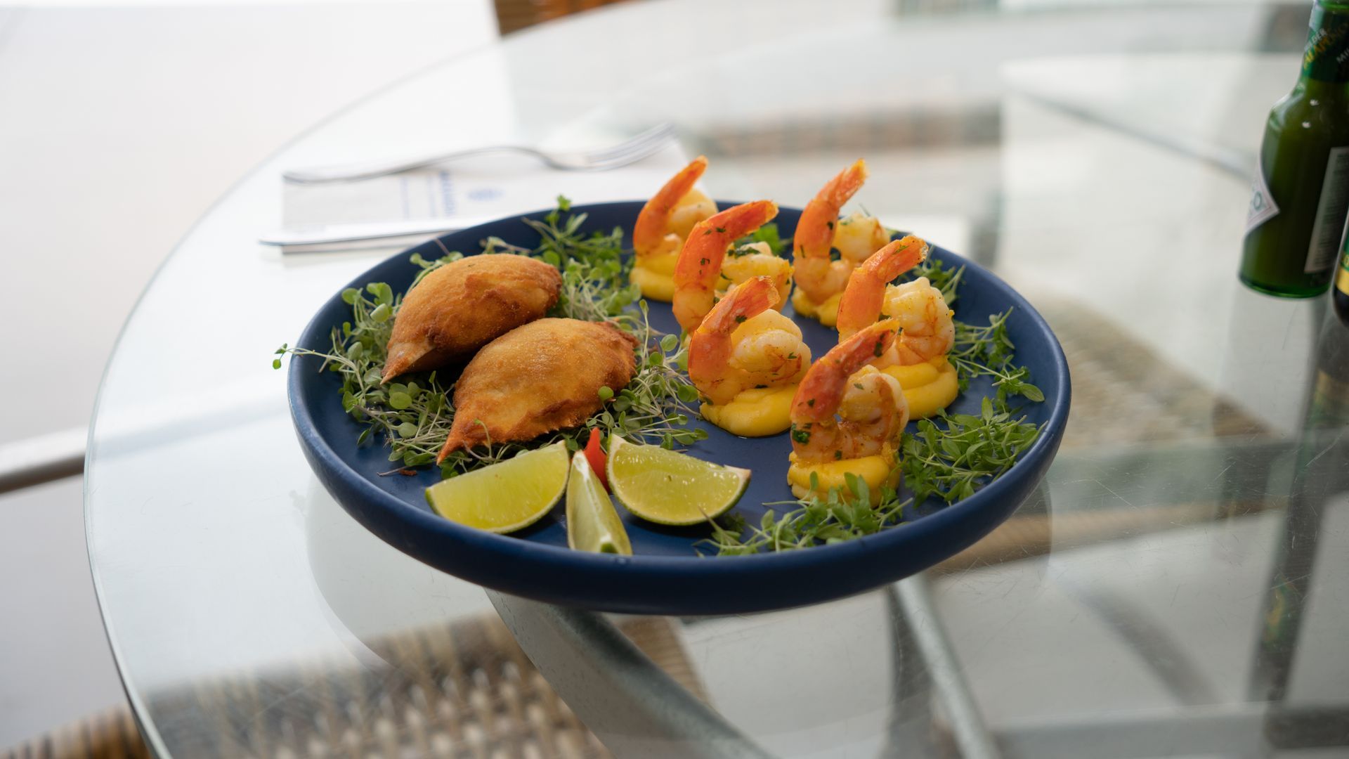 Prato gourmet de frutos do mar com camarão, peixe e verduras, servido em uma mesa de vidro.