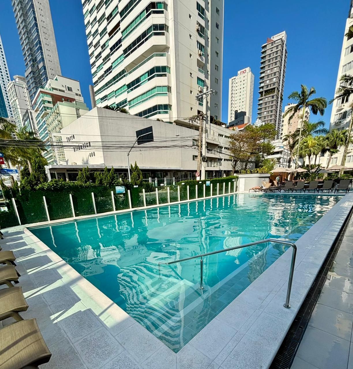 Piscina externa de hotel ao lado de prédios altos em um dia ensolarado.