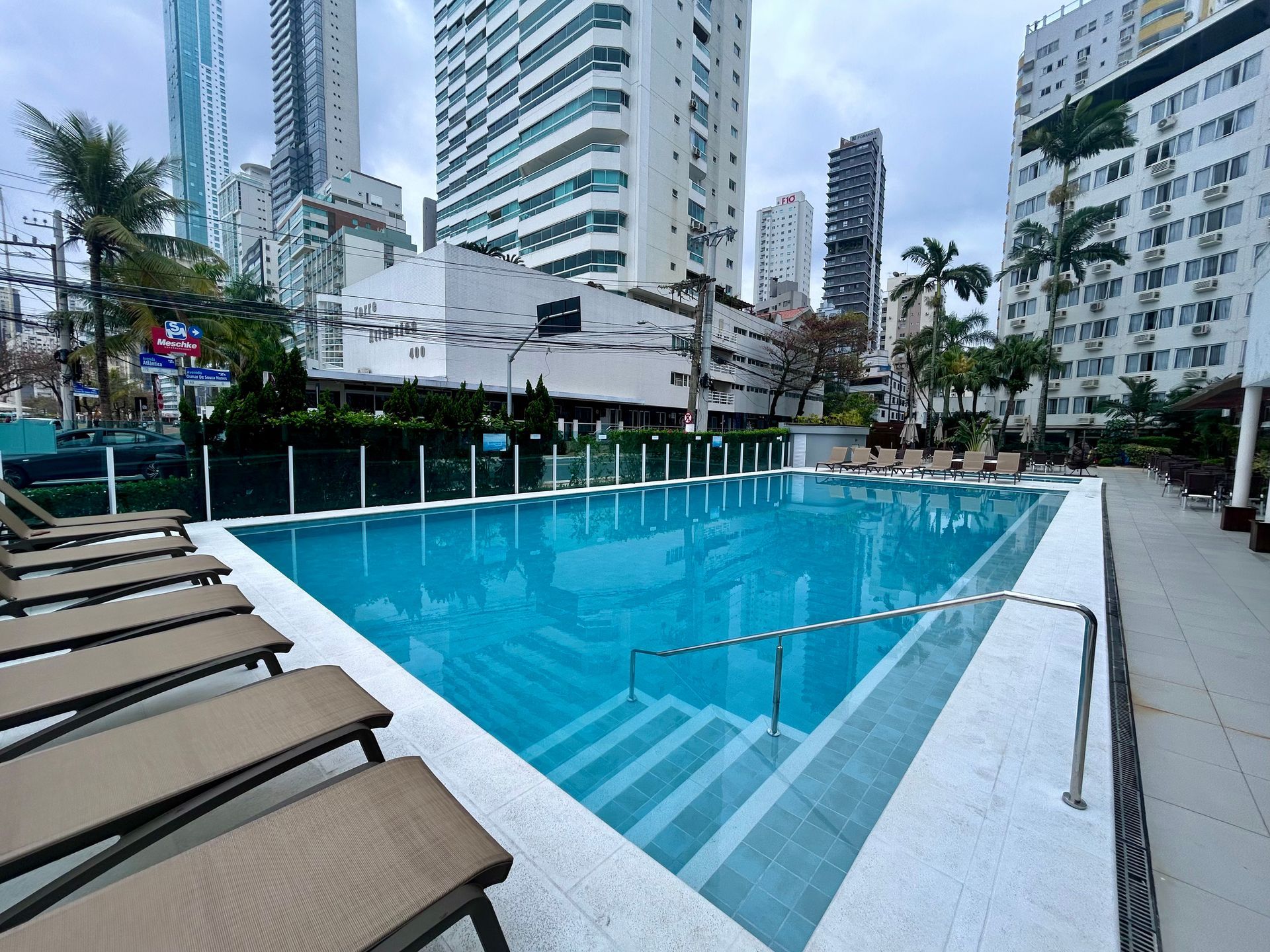 Piscina externa do hotel com água turquesa, espreguiçadeiras e arranha-céus da cidade ao fundo.