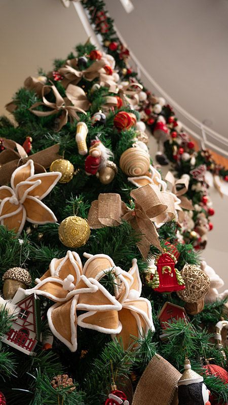 Árvore de Natal decorada com laços de fita dourada, enfeites e detalhes festivos em vermelho e branco.