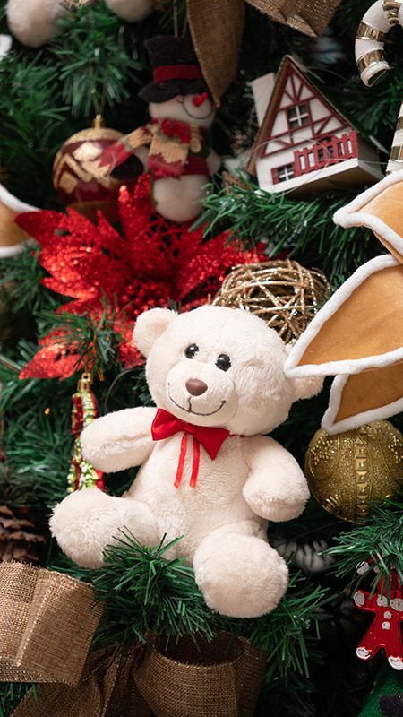 Enfeite de urso de pelúcia branco com fita vermelha em uma árvore de Natal com decorações vermelhas e douradas