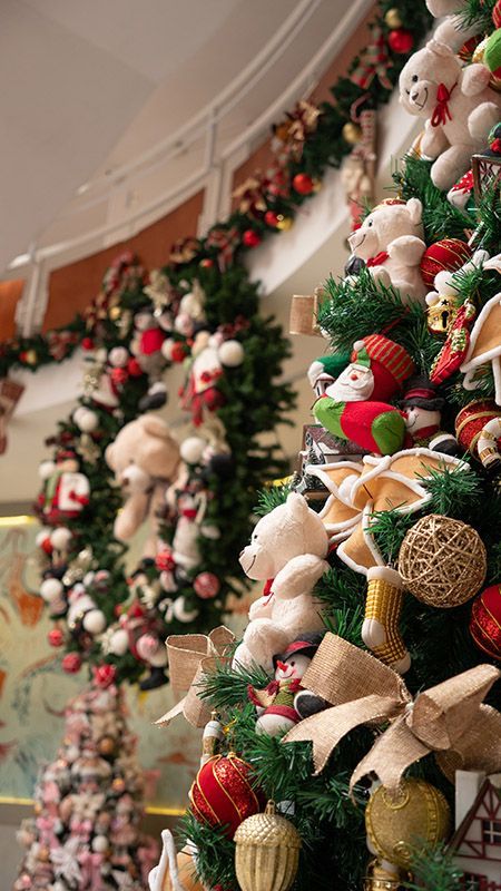 Guirlandas festivas com enfeites, laços e ursinhos de pelúcia decorando uma parede curva.
