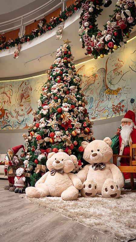 Decoração natalina com árvore decorada, ursinhos de pelúcia e figura do Papai Noel em um ambiente interno festivo.