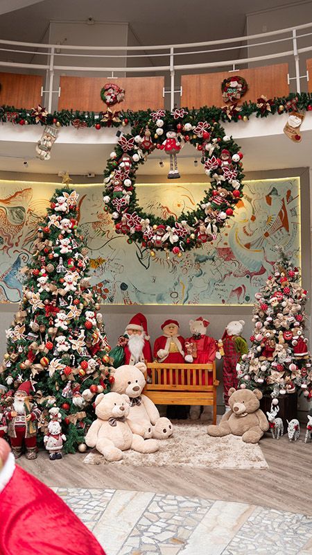 Hall de entrada festivo com árvores de Natal decoradas, guirlandas, festões, ursinhos de pelúcia e uma representação do Papai Noel.