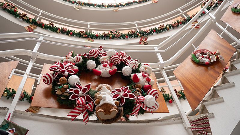 Átrio festivo de shopping center com bengalas de doces gigantes, decorações de biscoito de gengibre e guirlandas natalinas nas varandas.