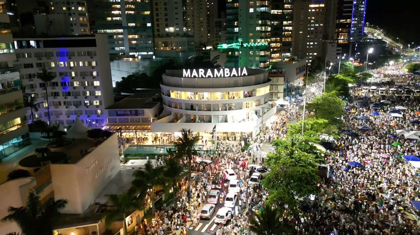 Protesto noturno de rua em frente a um prédio iluminado em Marambaia, com uma grande multidão ocupando a rua.