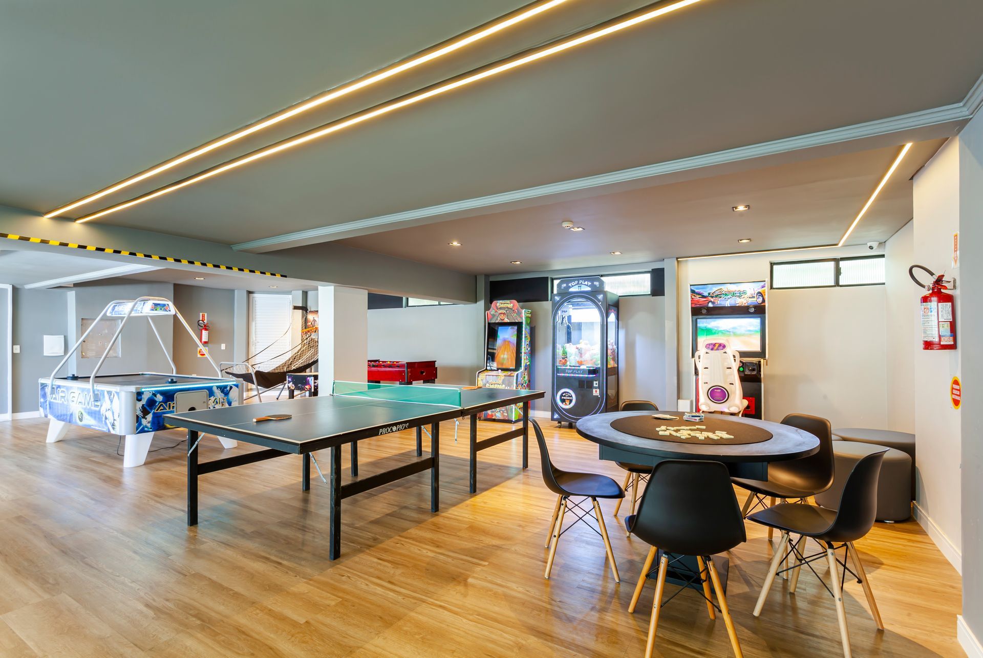 Sala de estar moderna com mesa de pingue-pongue, área de estar, piso de madeira e iluminação geral brilhante.