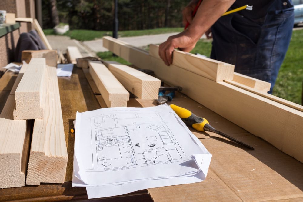 Person Measuring Wood Planks on a Workbench With a Floor Plan — C K Carpentry in Byron Bay, NSW