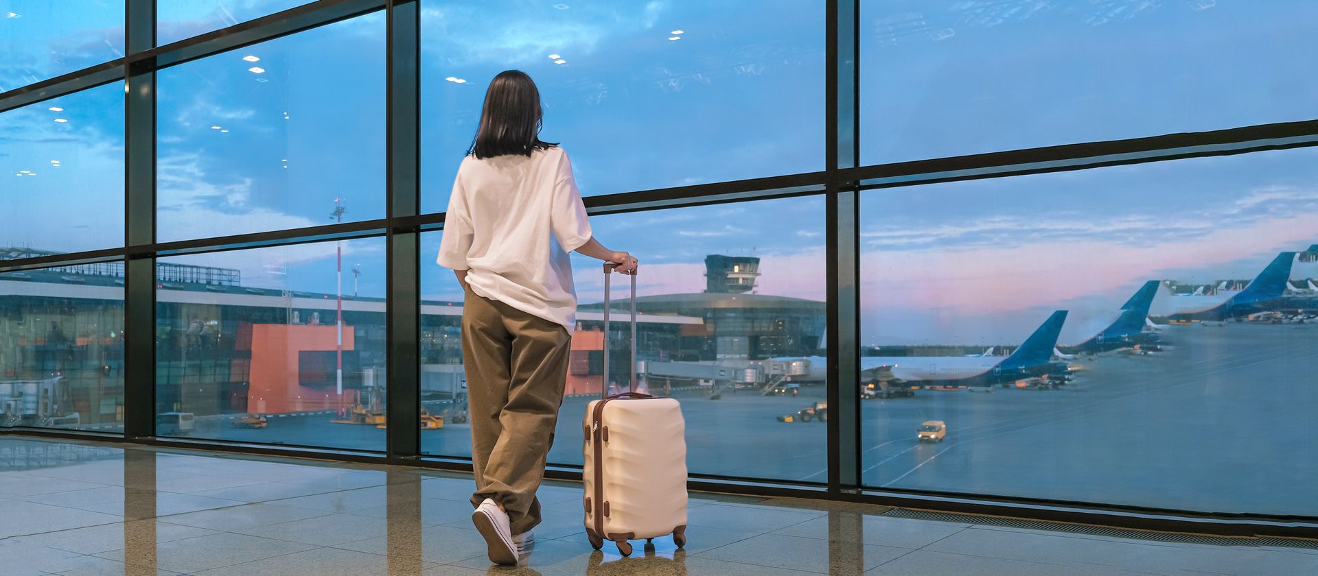 Traveler with a suitcase looking out through airport windows at planes and a waterfront skyline