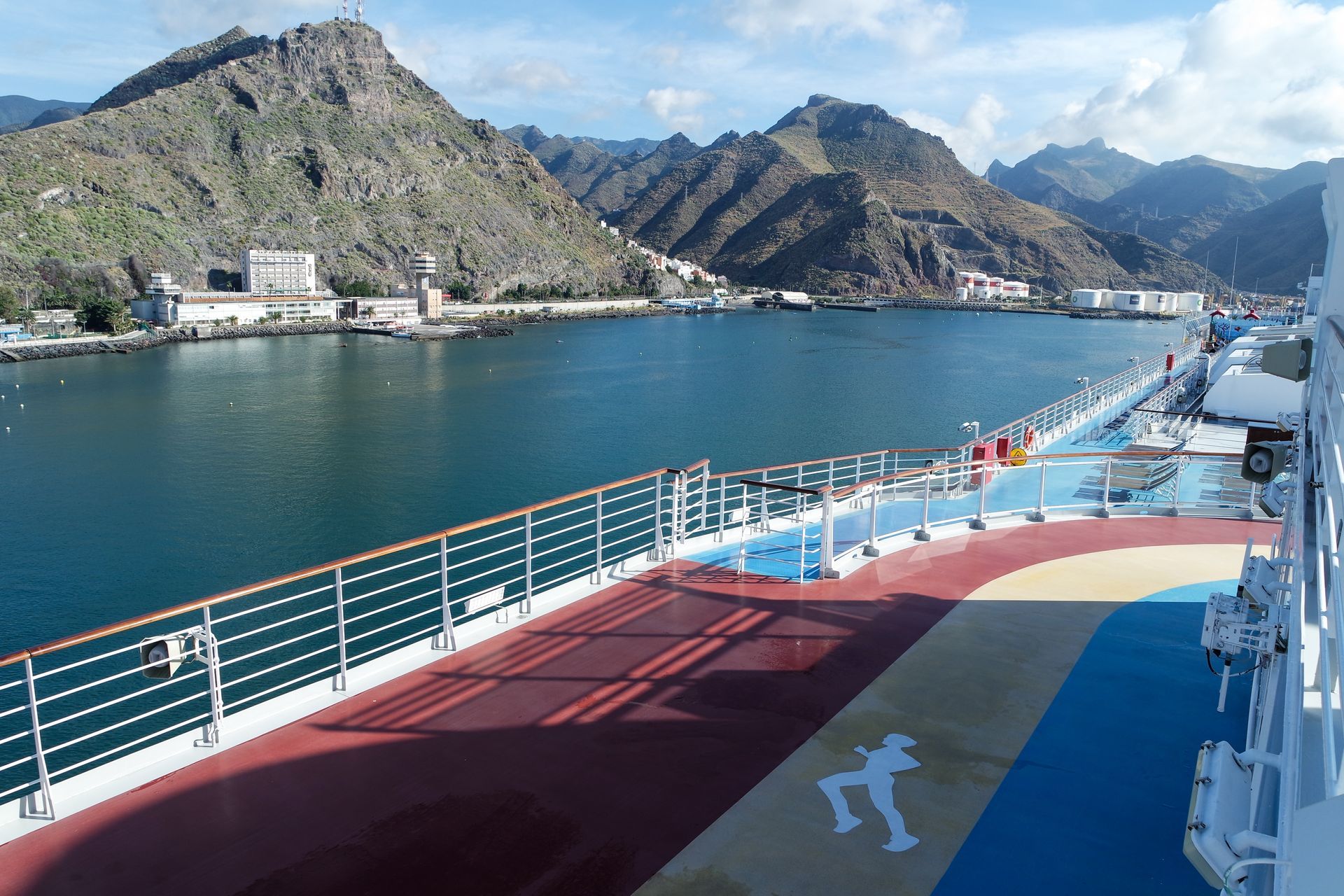 Cruise ship deck overlooking a calm blue bay and rocky mountains under a clear sky