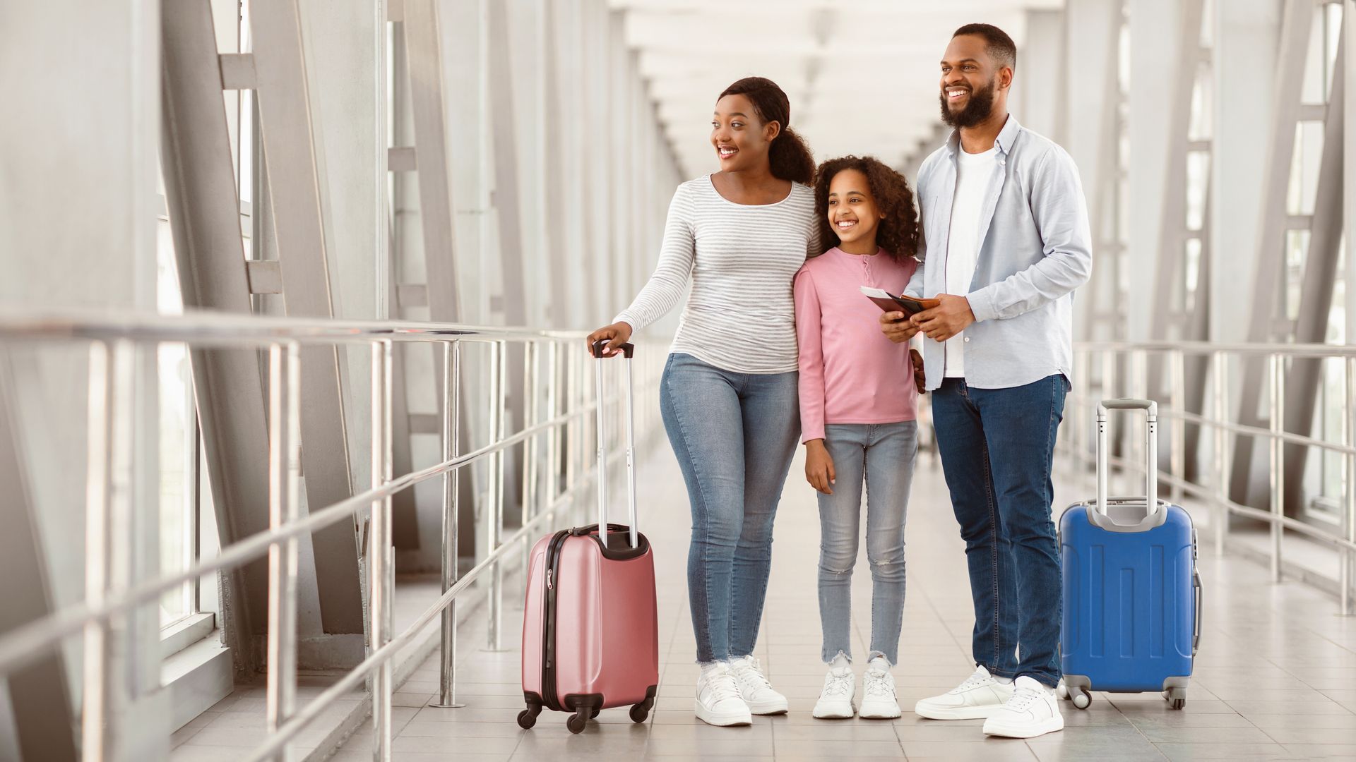 Family with luggage walking through an airport corridor, smiling and holding hands