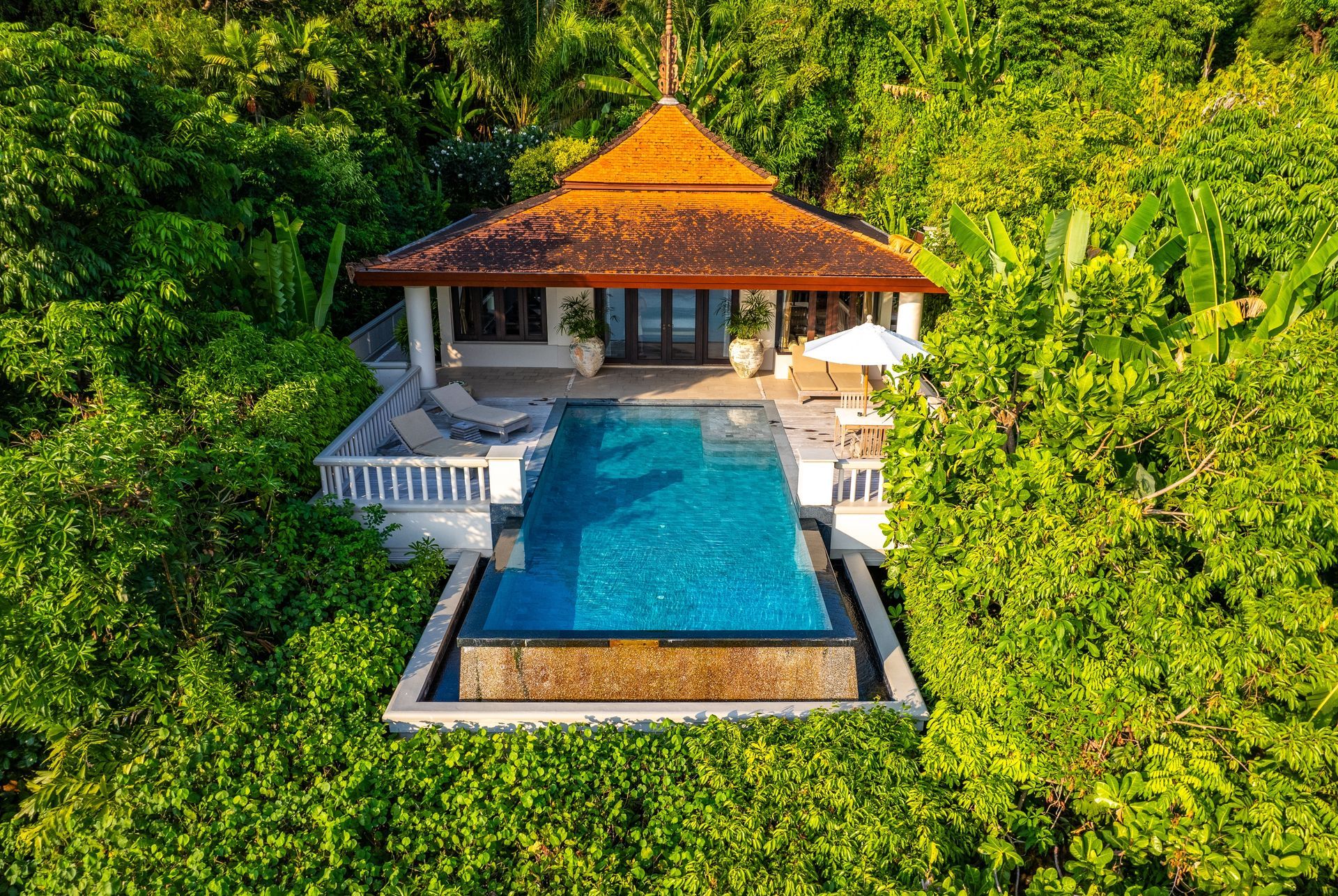 Tropical villa with a blue pool, orange-tiled roof, and lush green surrounding jungle