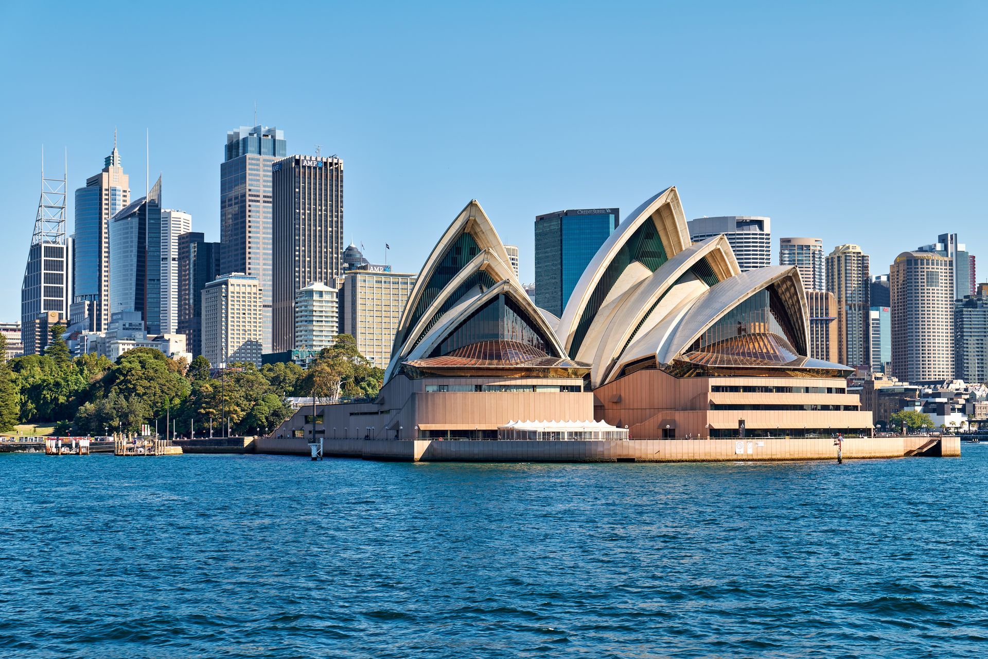Sydney Opera House with harbor water and city skyline under a clear blue sky