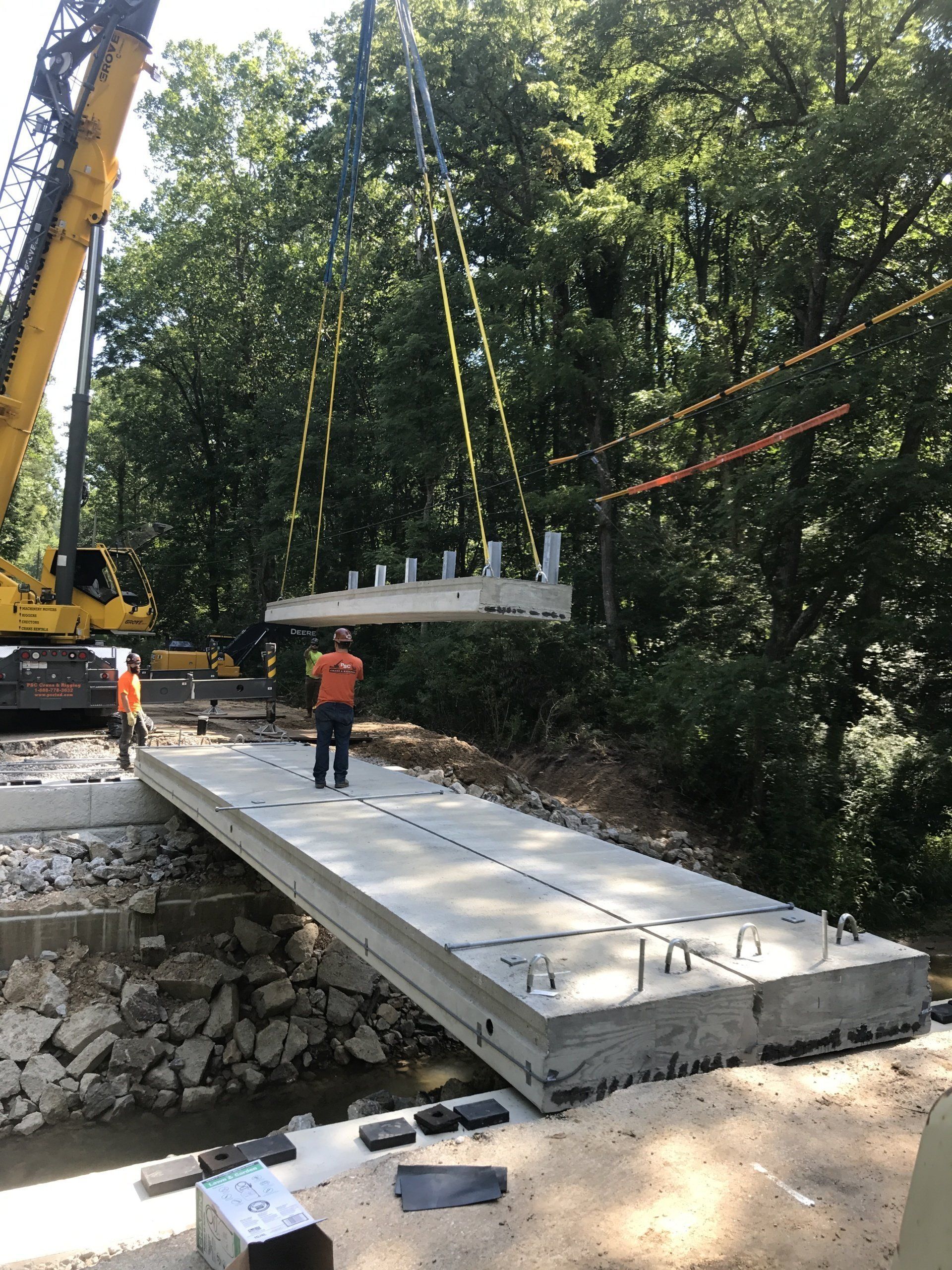 A crane is lifting a concrete bridge over a river