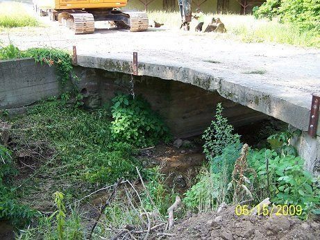 A bridge over a stream with a yellow excavator in the background