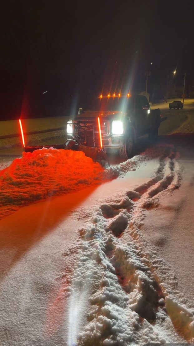 Pickup truck with headlights on in a snowy roadside ditch at night, tire tracks visible in the snow.