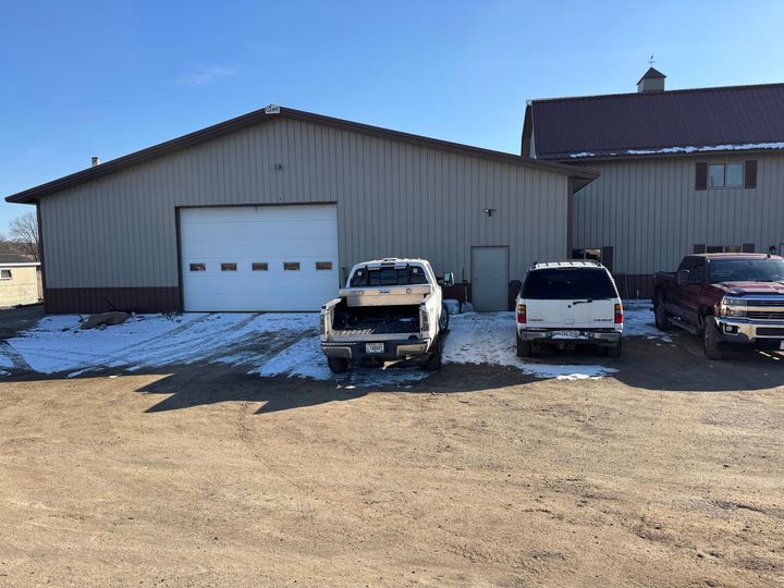 Snowy farmyard with a tan metal garage and three parked vehicles in front.