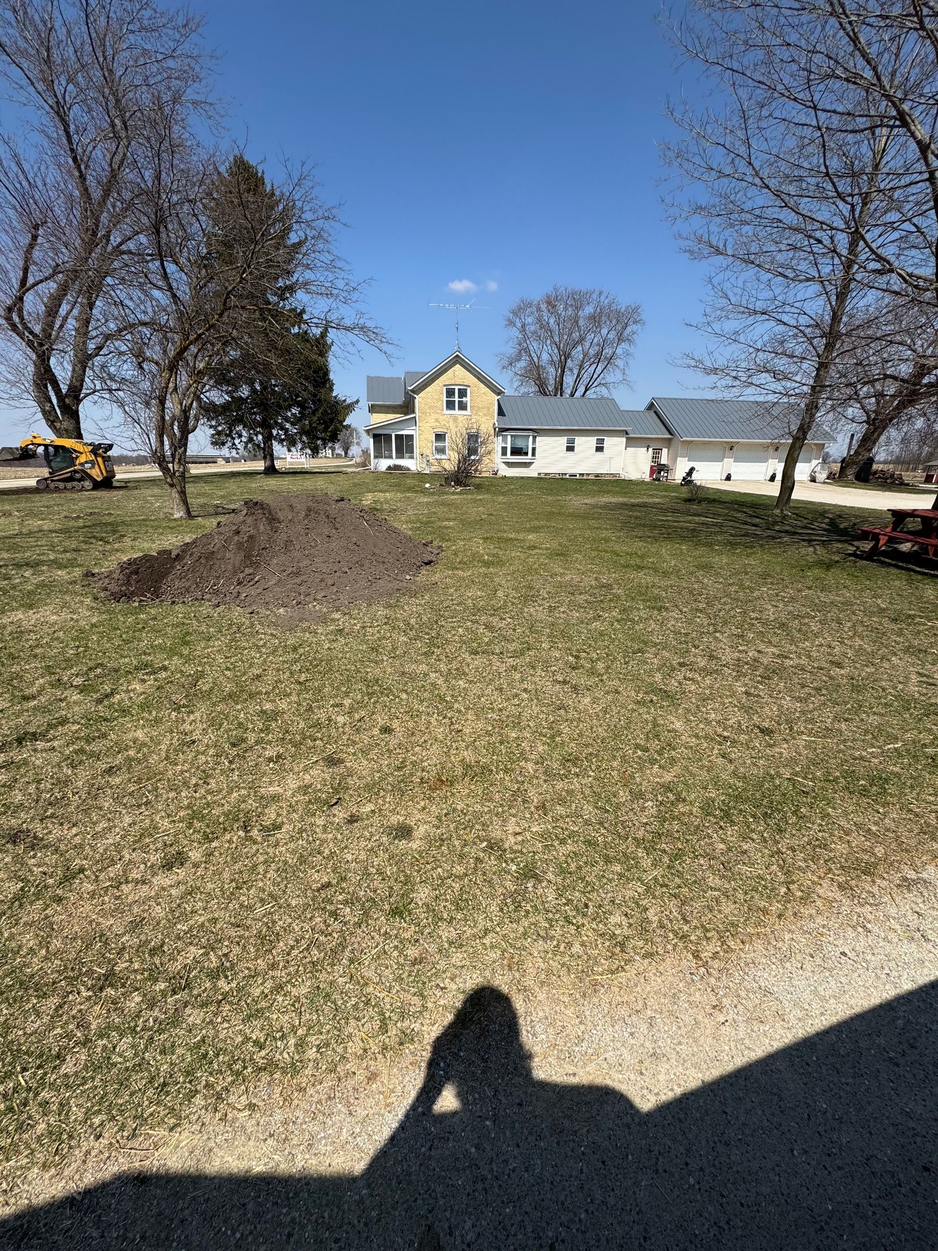 Grassy yard with trees and a yellow house under a clear blue sky