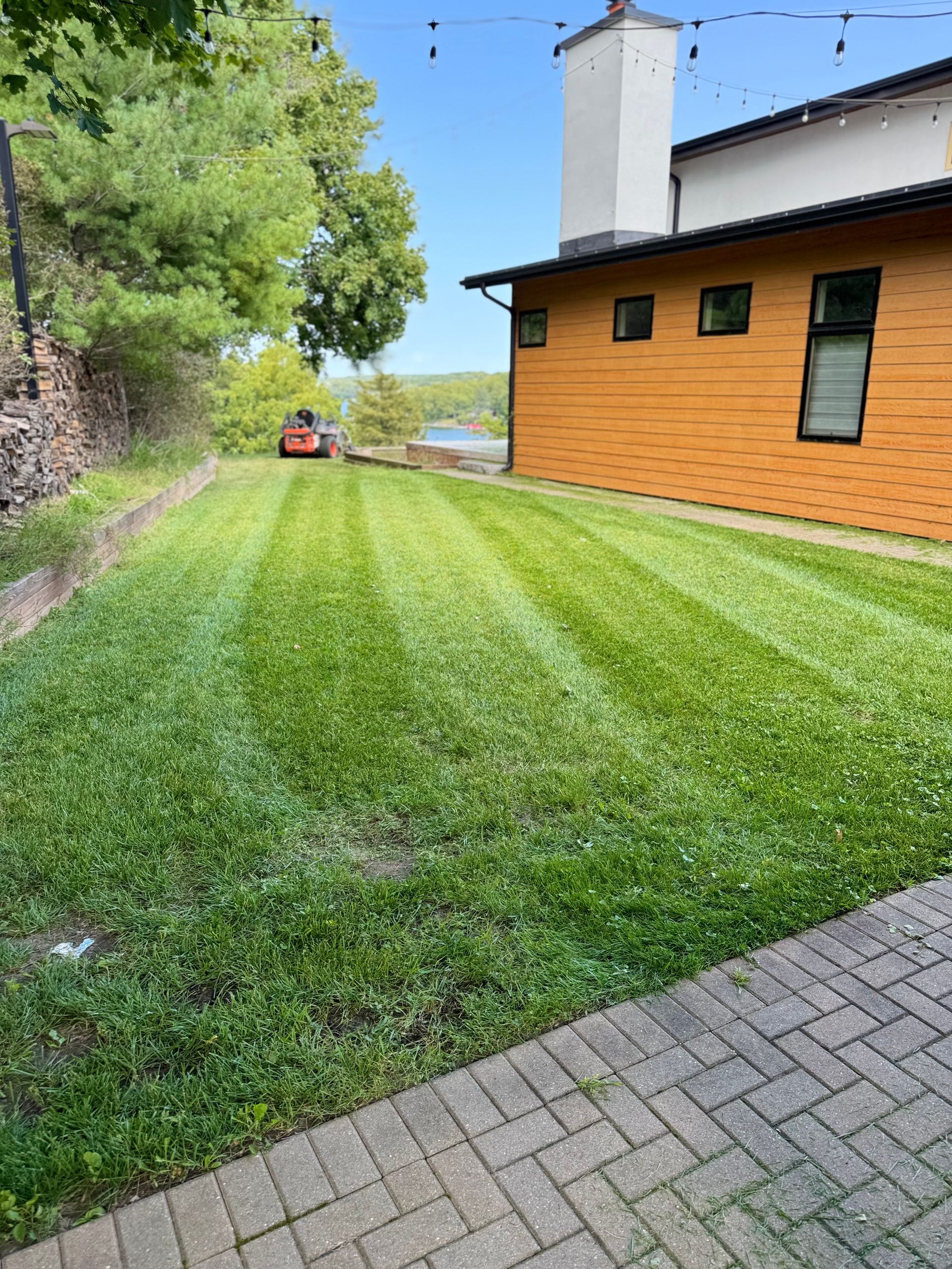 Freshly mowed green lawn beside an orange house with a stone path and wooded slope nearby