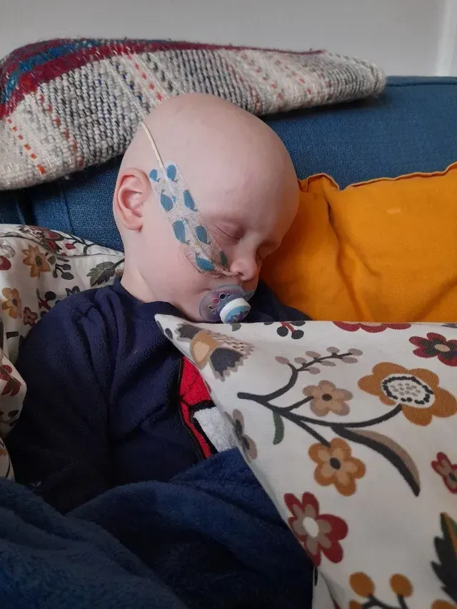 Child sleeping on a couch under blankets, with a colorful butterfly face paint design.
