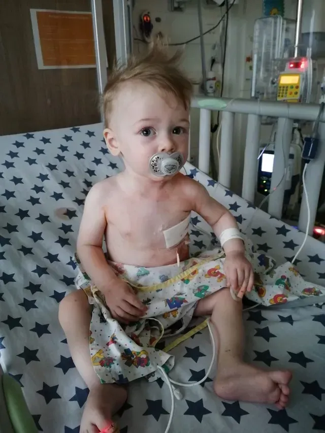 Baby sitting in a hospital bed with a pacifier and medical monitoring equipment nearby