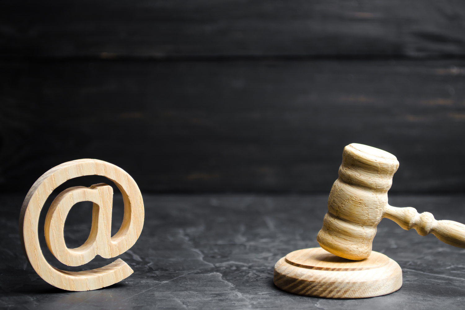 Wooden @ symbol beside a judge’s gavel on a dark tabletop