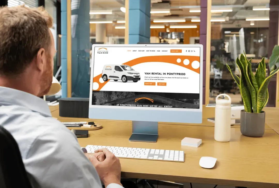 Person at a desk viewing a car website on a desktop computer in an office setting