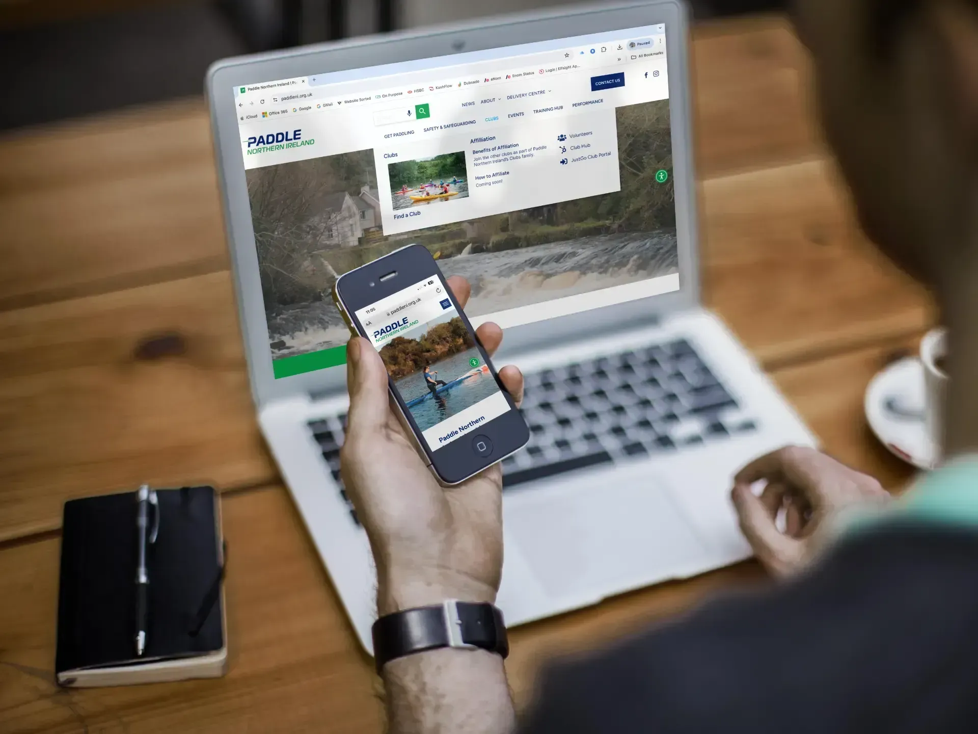 Person using a smartphone in front of a laptop with a website open on the screen