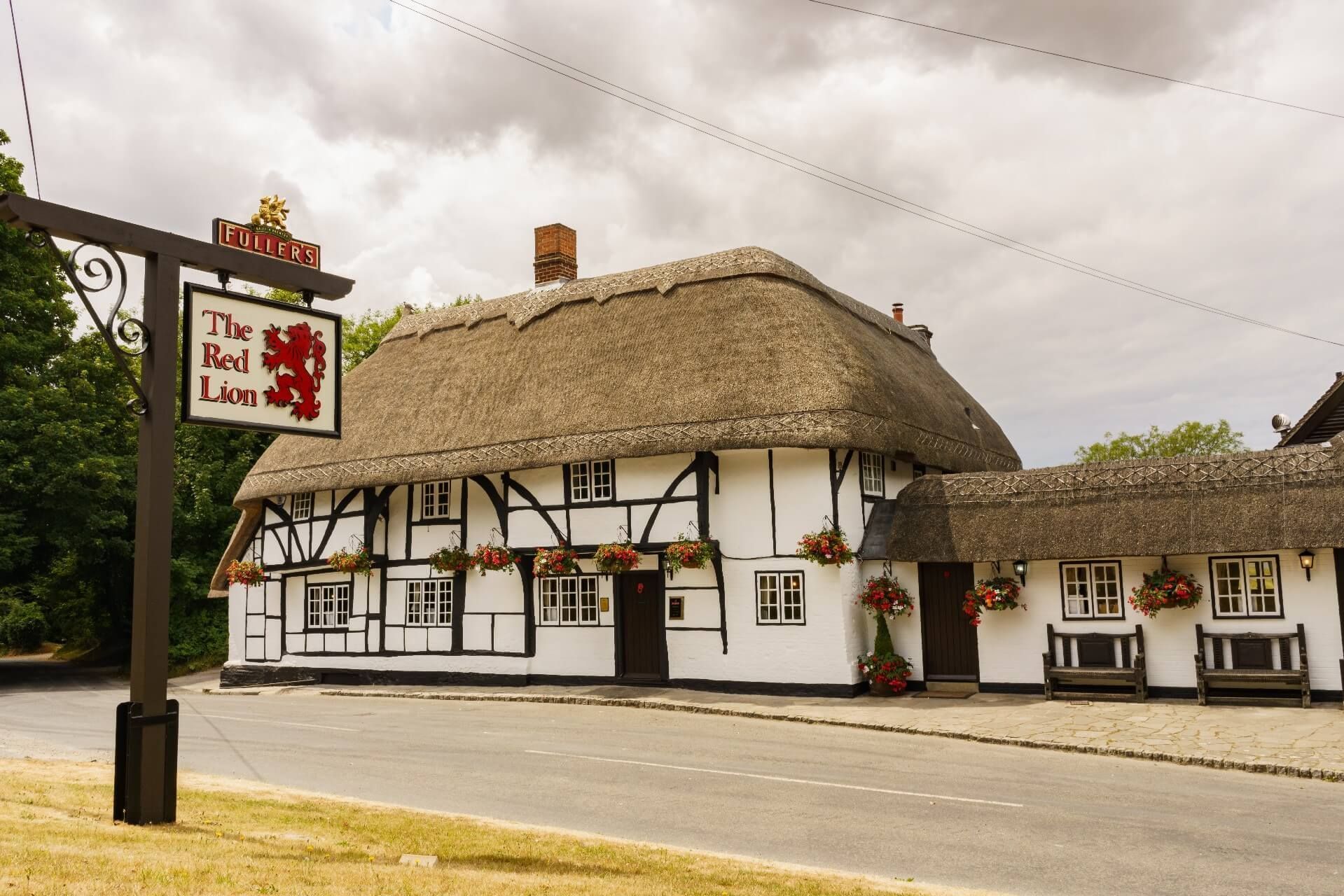 Thatched white Tudor-style inn with a red sign on a quiet roadside