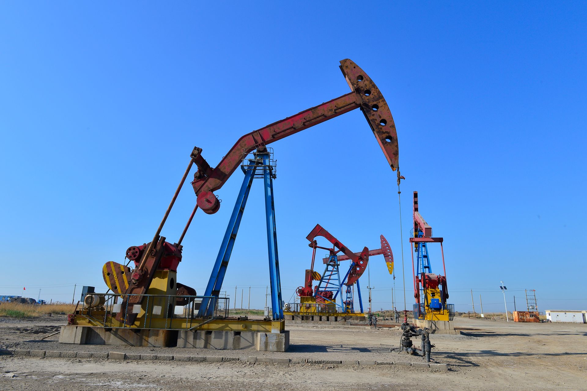 Oil pump jacks extracting crude petroleum at an active oilfield under clear blue sky. Oil pump jacks extracting crude petroleum at an active oilfield under clear blue sky.