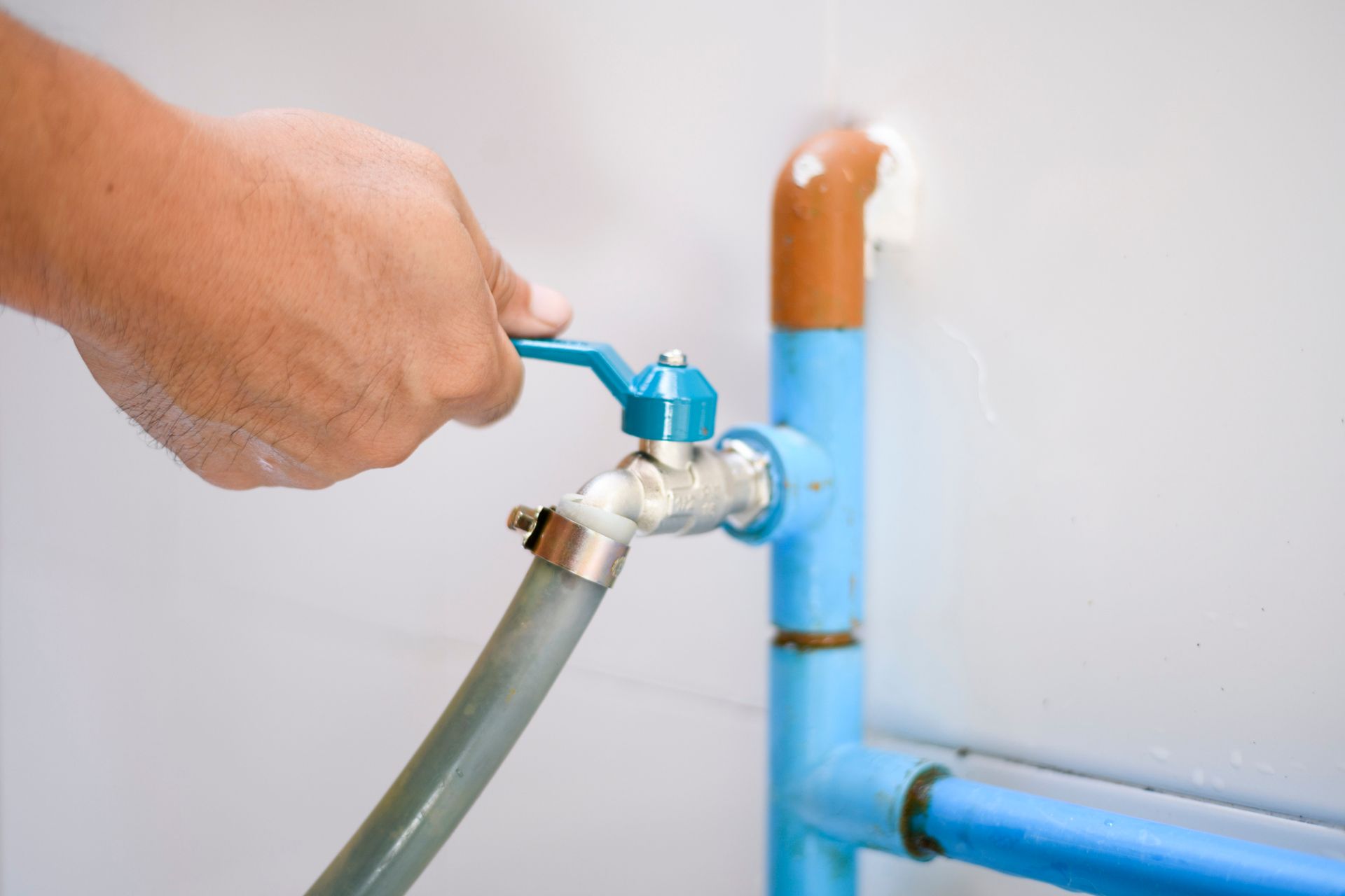 A hand opens the blue faucet of a blue pipe. A hand opens the blue faucet of a blue pipe.