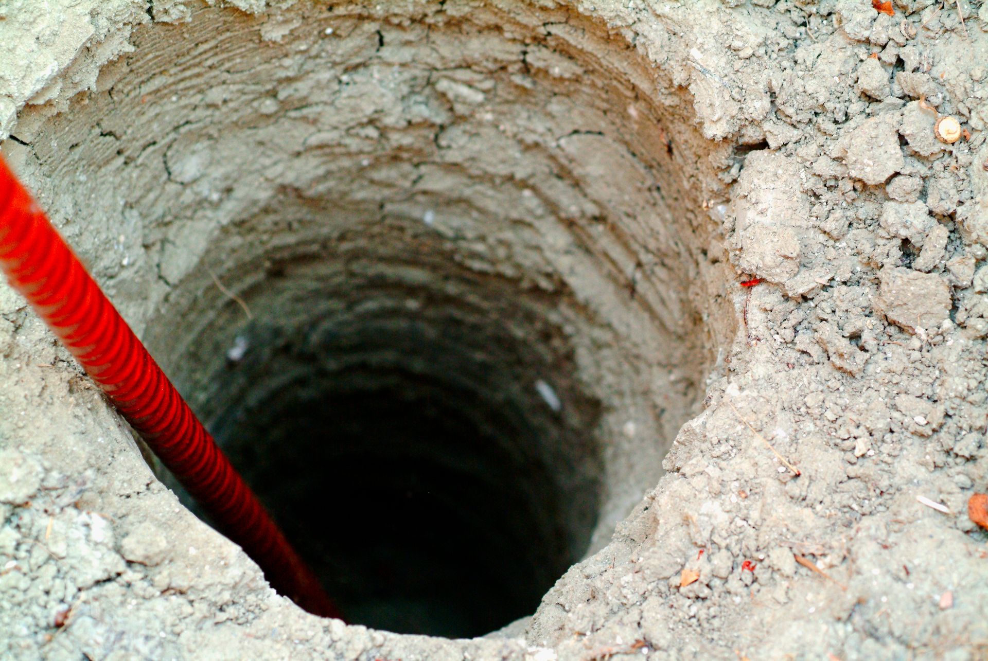 A hole in the ground with a red hose sticking out of it. A hole in the ground with a red hose sticking out of it.
