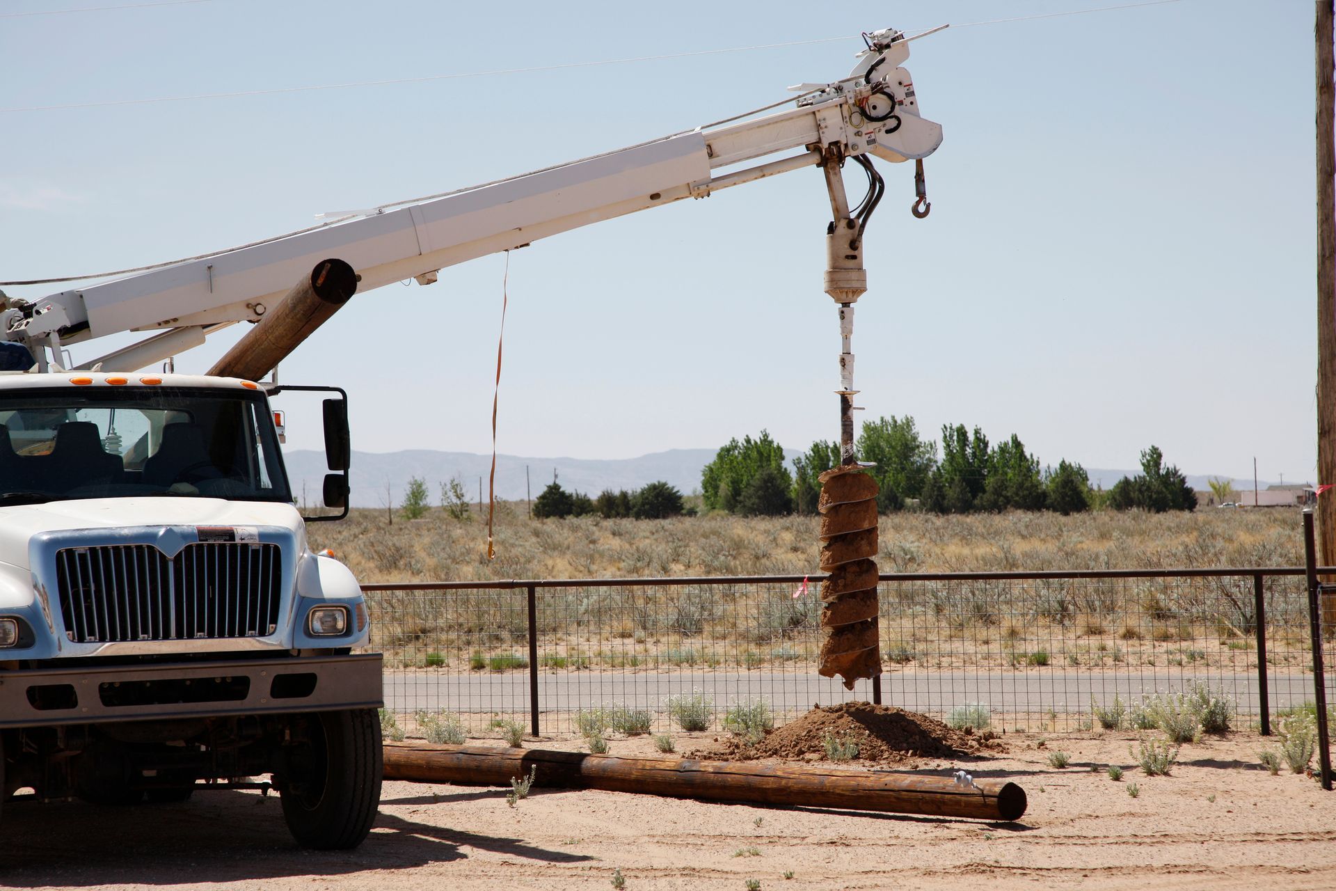 A white truck with a crane attached to it is parked in a field. A white truck with a crane attached to it is parked in a field.